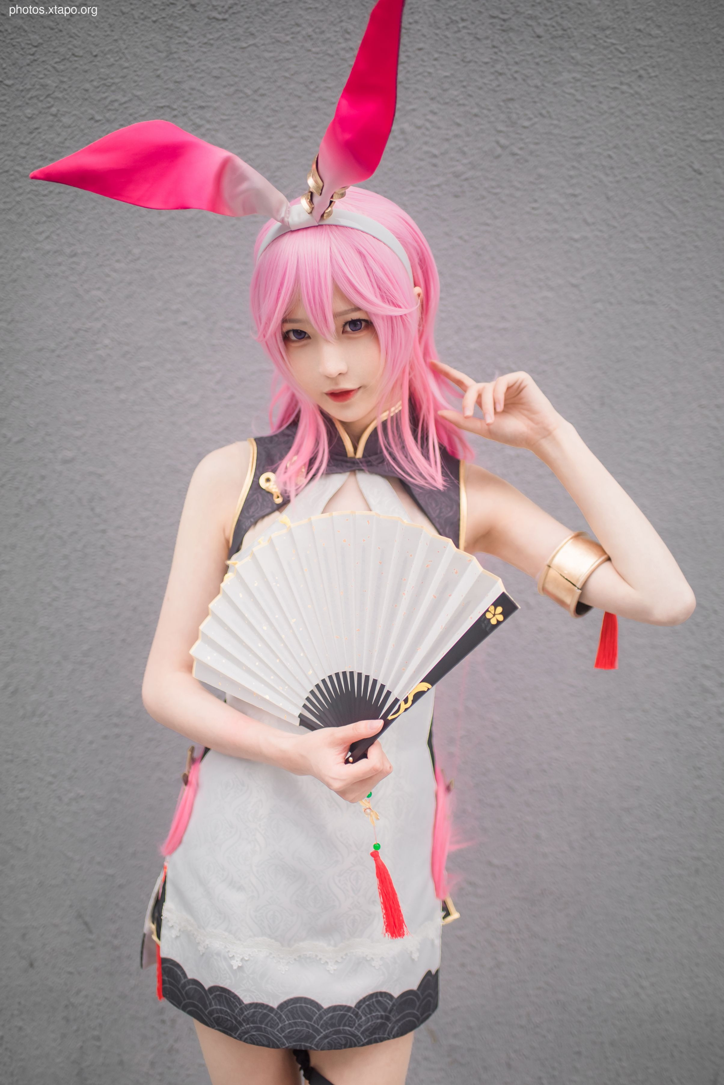 Cosplayer dressed in a pink and white outfit, bunny ears, and holding a white fan. The outfit is a modern take on traditional Chinese clothing.  