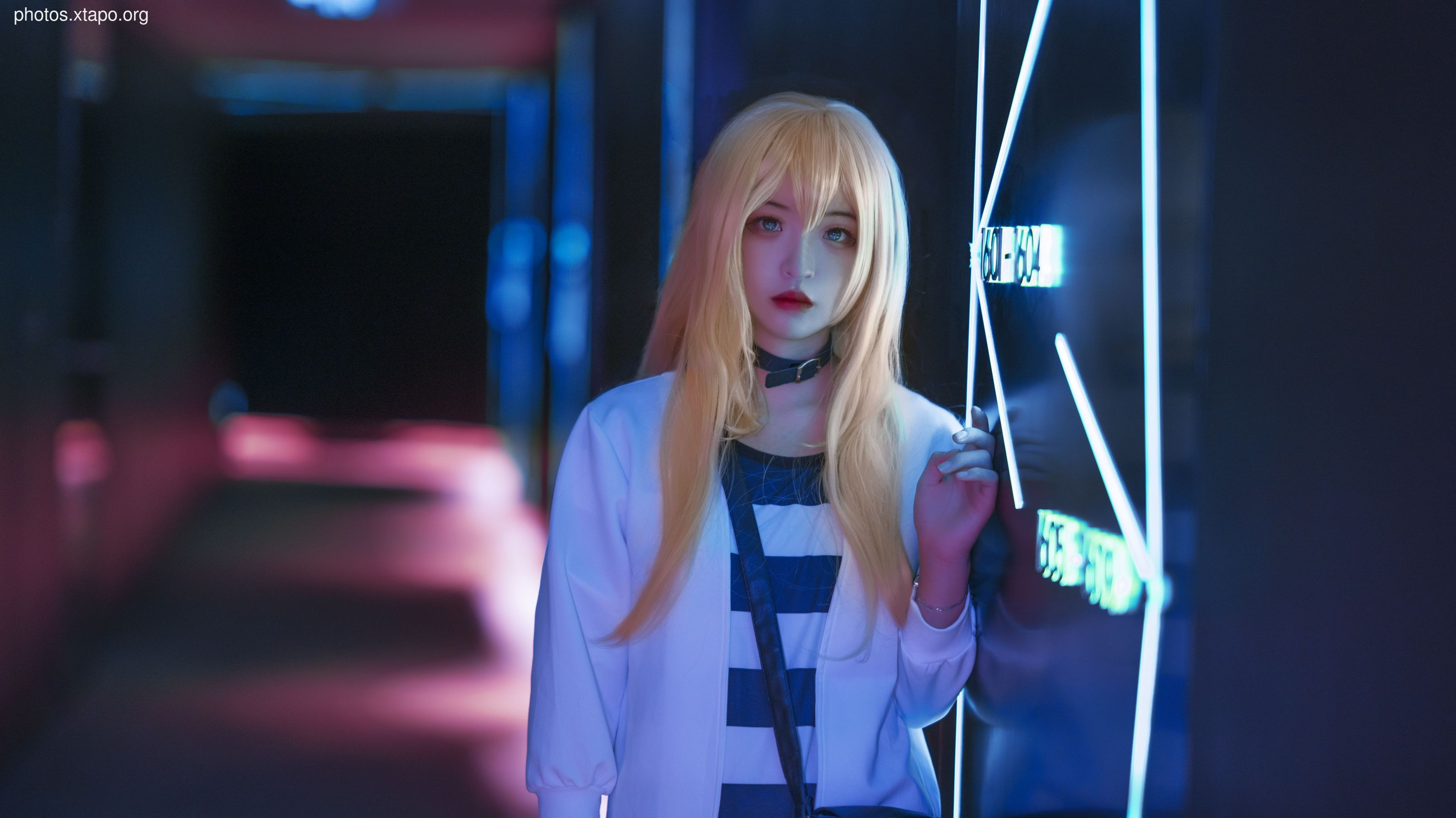 A young woman in a stylish cosplay outfit poses against a backdrop of vibrant neon lights. The image is evocative of futuristic settings found in anime and video games.