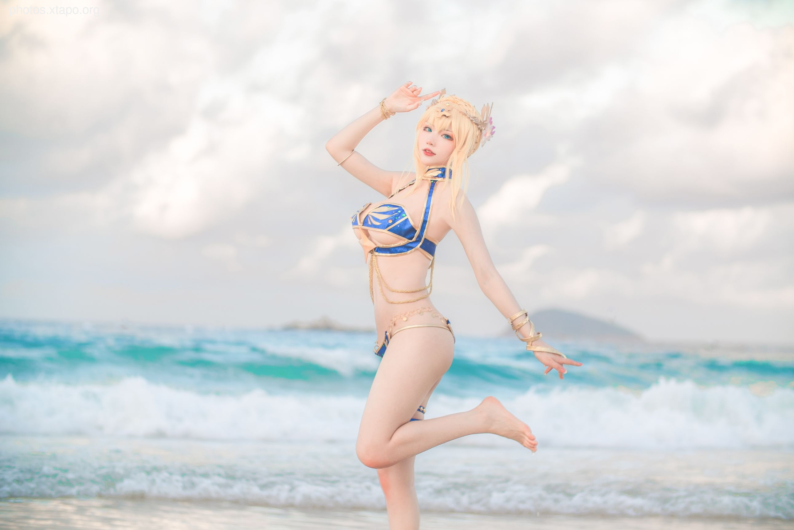 Cosplay photography of a woman in a blue and gold bikini on a beach.