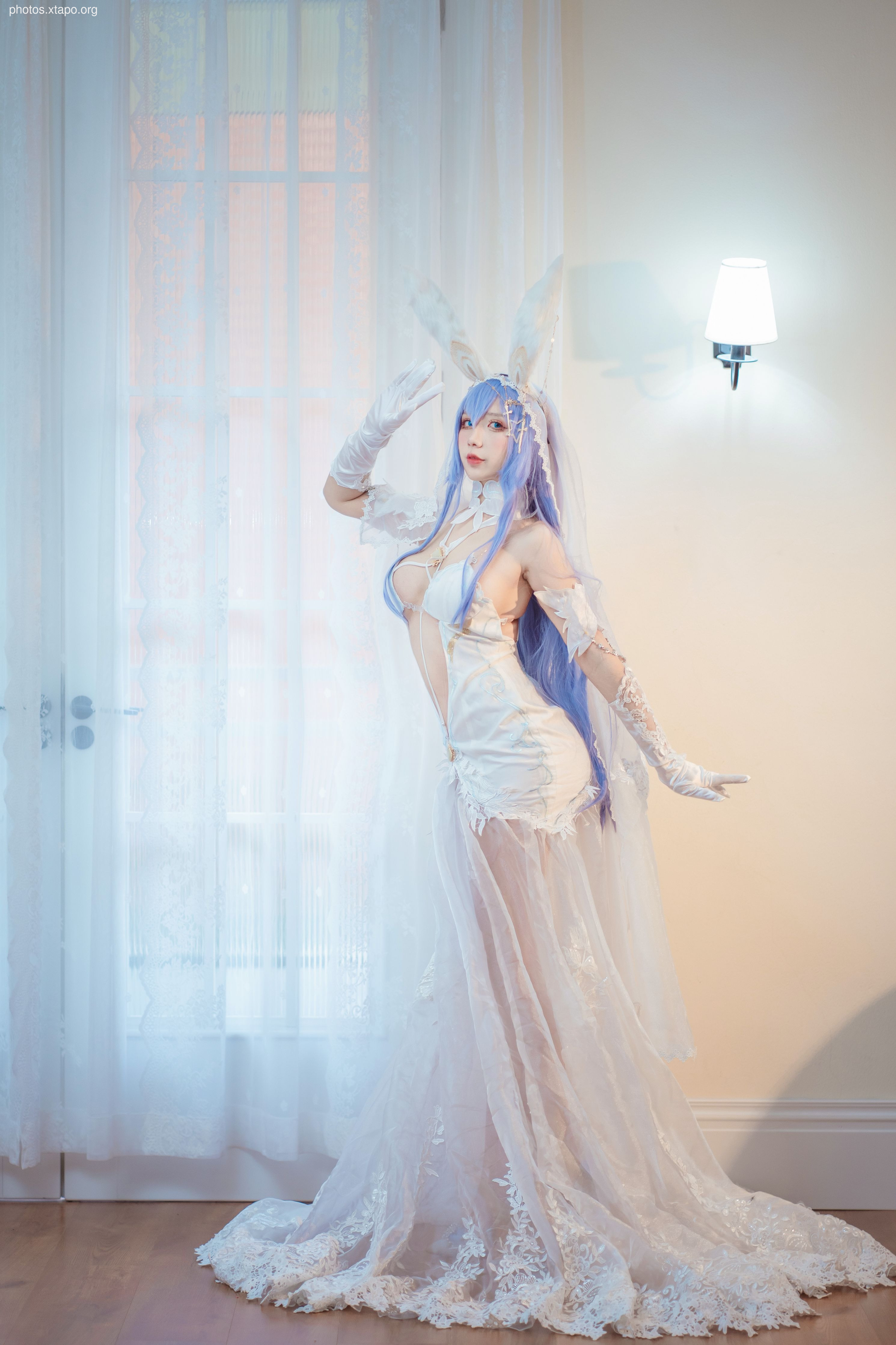 A stunning cosplayer in an elegant white wedding dress with long, flowing veil and bunny ears.