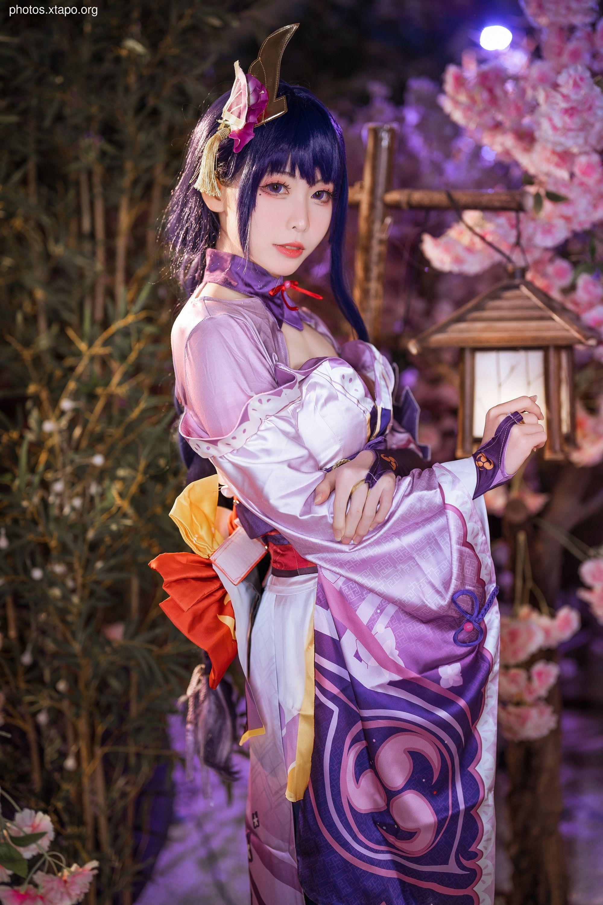 A stunning cosplay of an anime character in a vibrant purple kimono, adorned with intricate details and a unique headdress. The setting features blooming cherry blossoms, enhancing the ethereal beauty of the image.