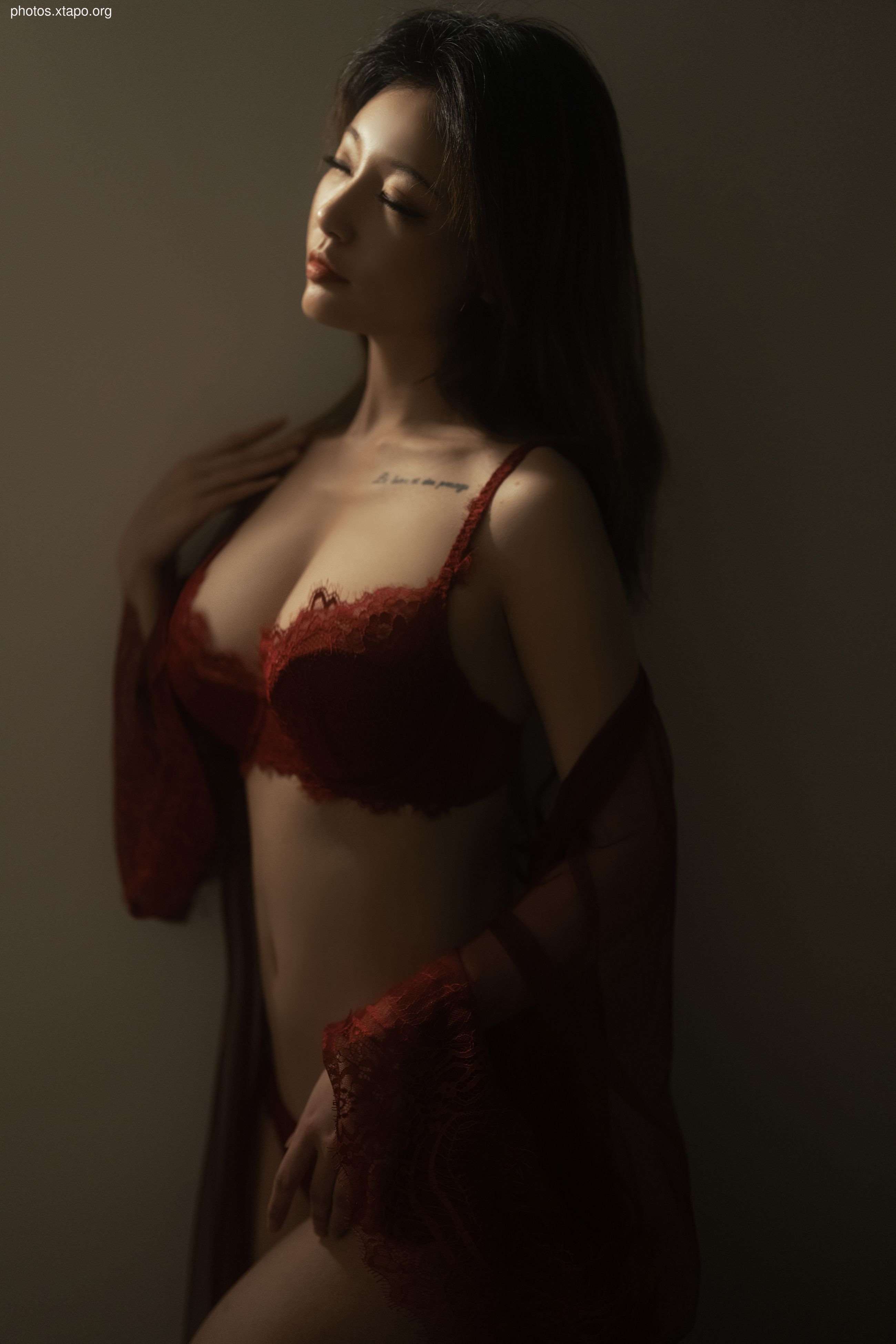 A woman poses in red lingerie, her eyes closed in a moment of peaceful sensuality.
