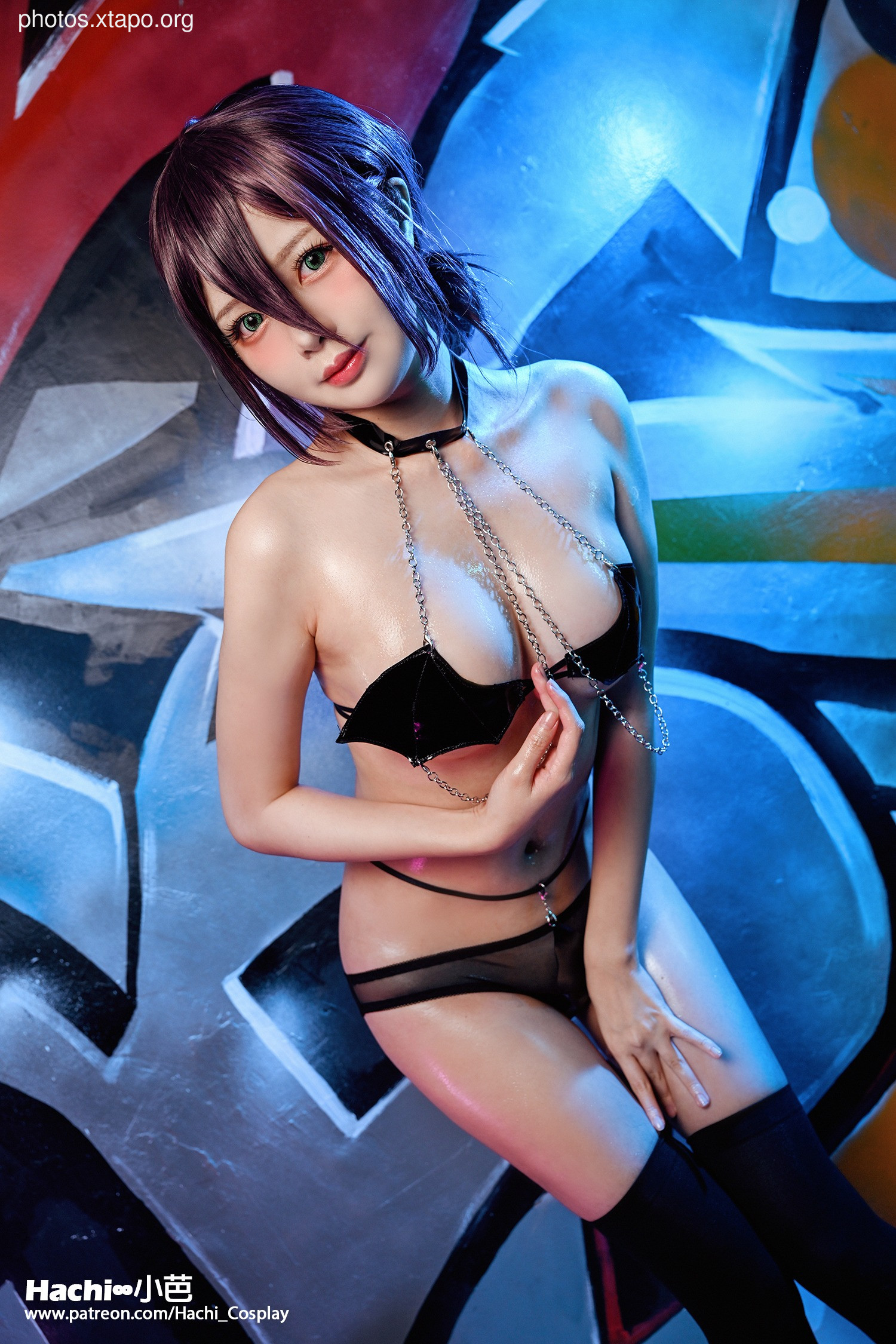 A striking image of a cosplay model posing in a revealing black outfit against a graffiti backdrop. The model's dark hair and intense gaze add to the overall aesthetic.