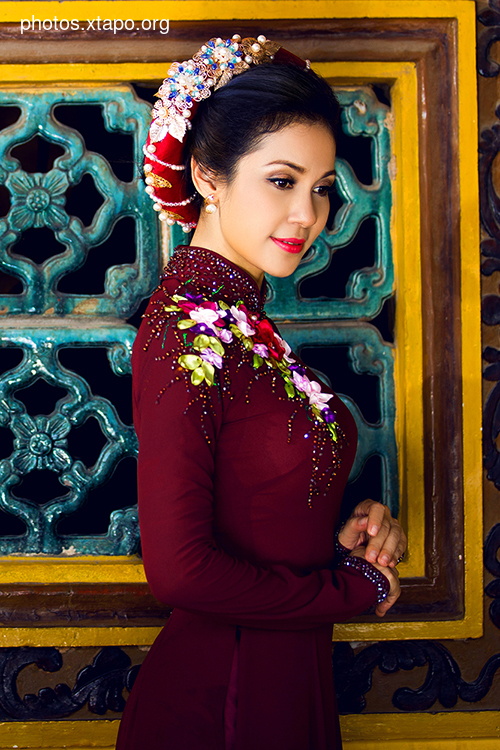 A young woman in a stunning crimson Ao Dai, adorned with intricate floral embroidery and a beautiful headpiece. The traditional Vietnamese dress is beautifully complemented by the ornate background.