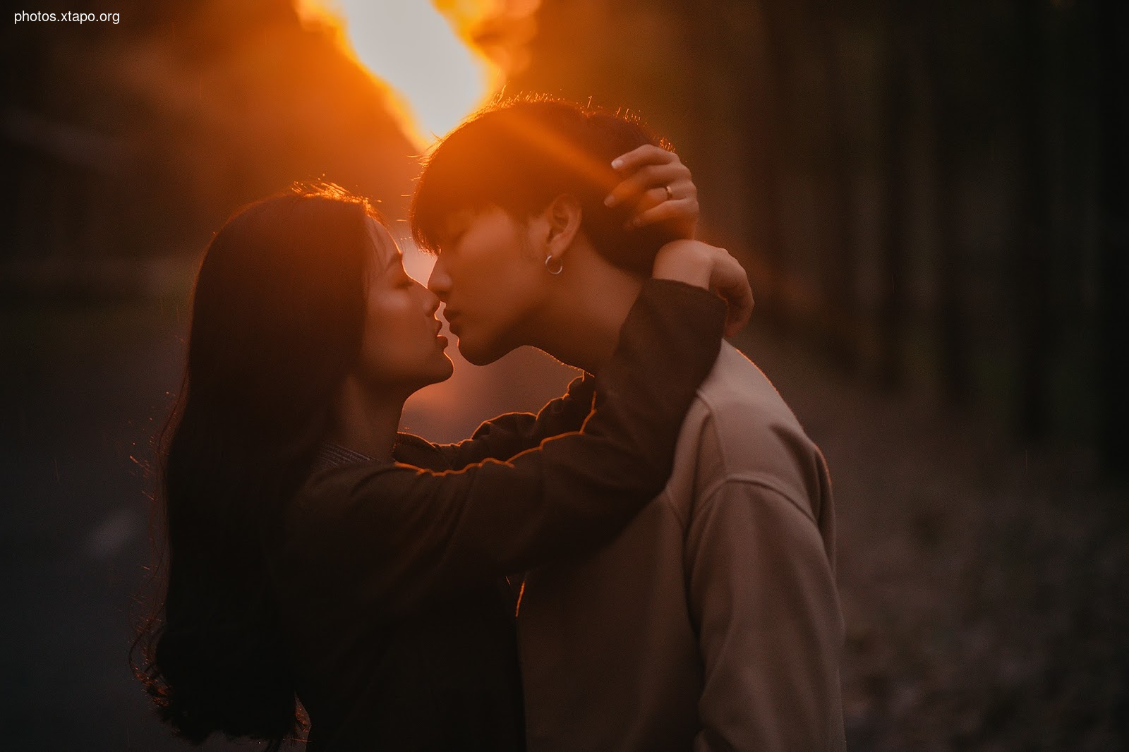 A couple shares a passionate kiss as the sun sets in the background.