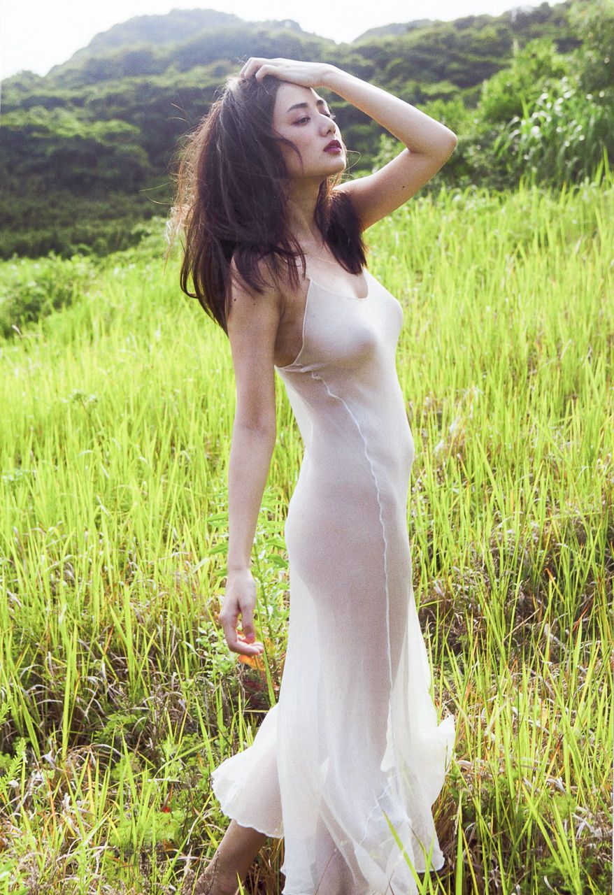 A woman in a sheer white dress stands in a field of tall grass.