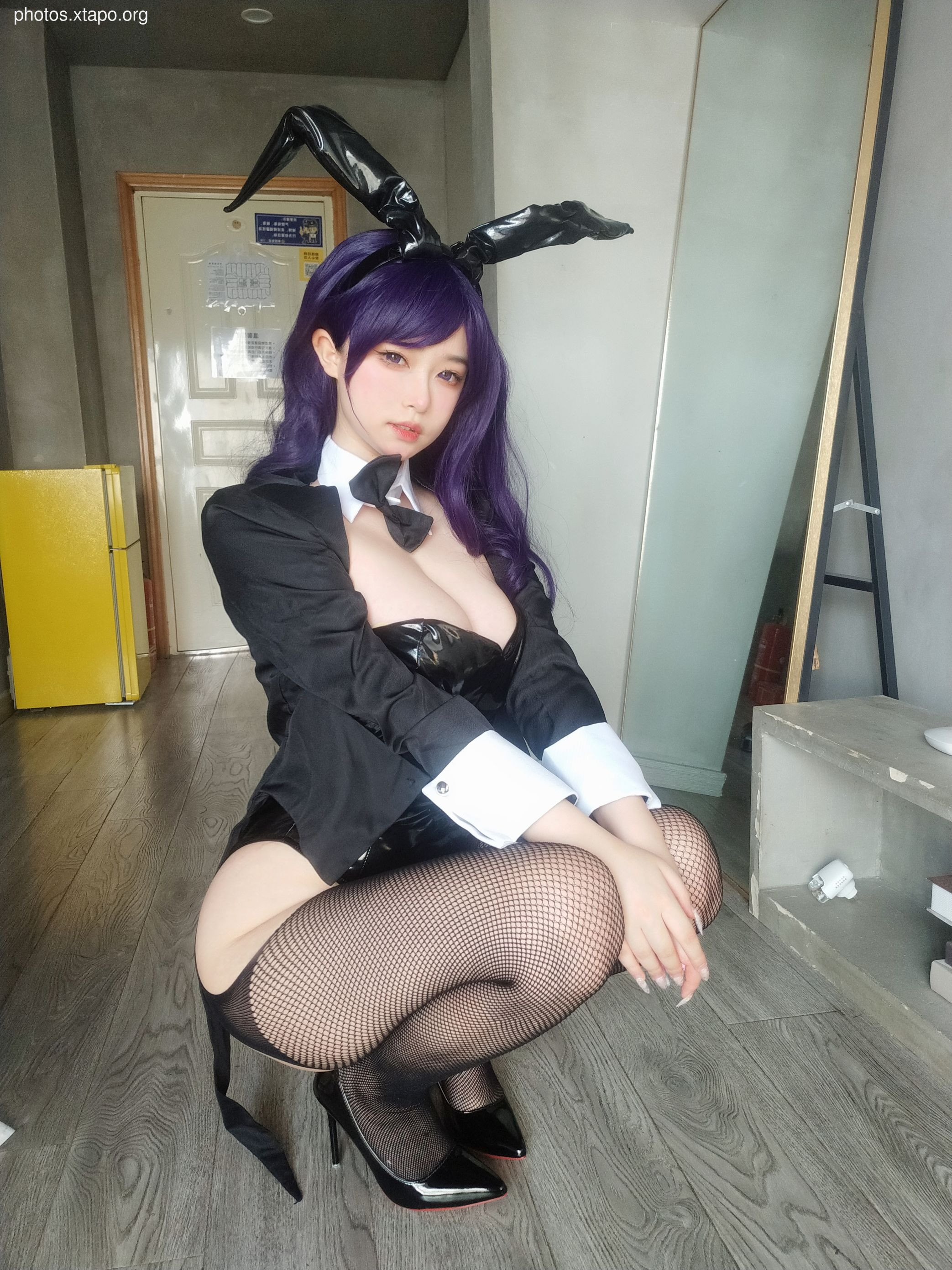 A woman in a black bunny girl costume with purple hair poses for a photo.
