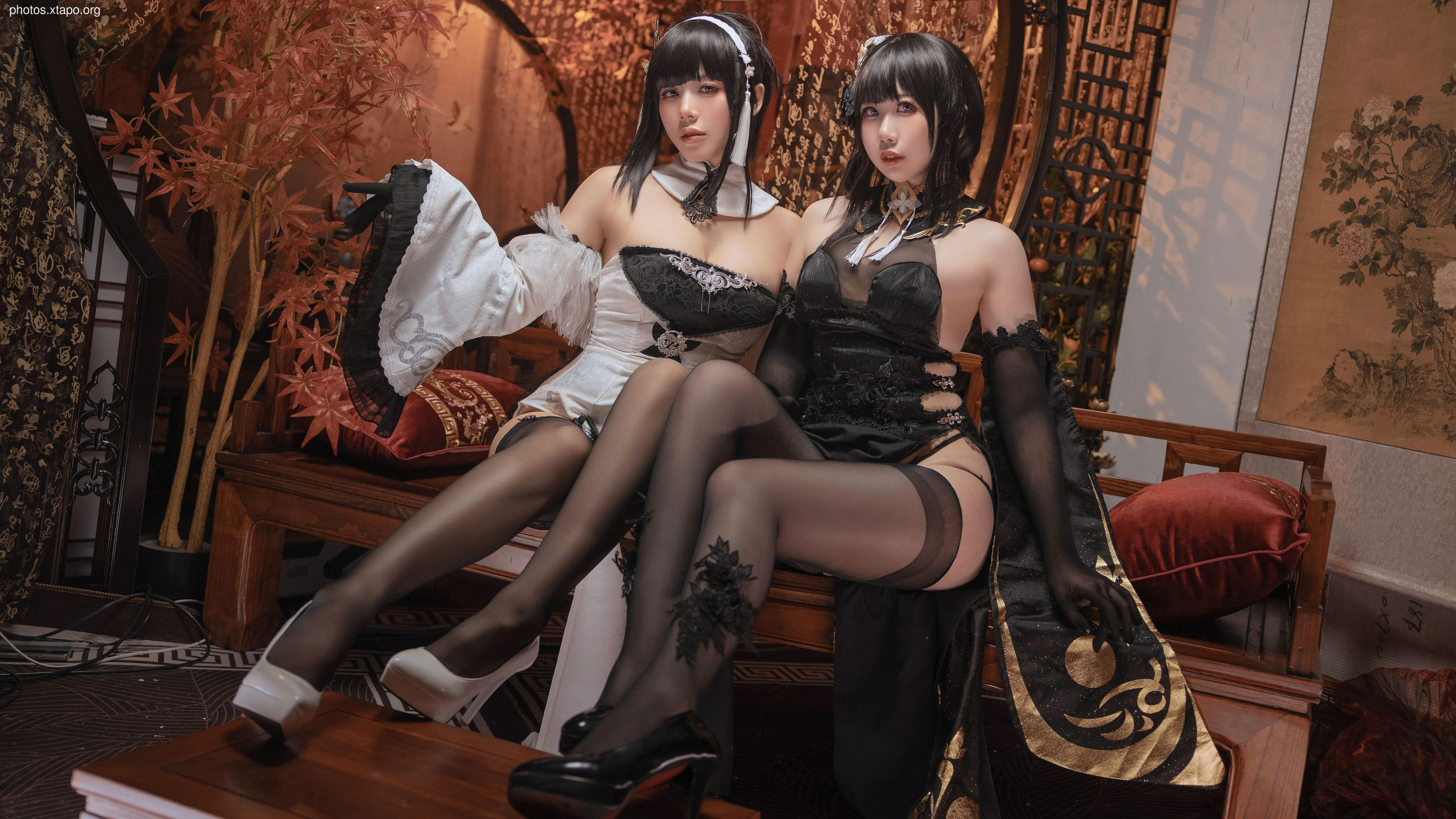 Two women in elaborate cosplay costumes, one in white and one in black, pose for a photo.  The setting is reminiscent of a traditional Chinese interior.