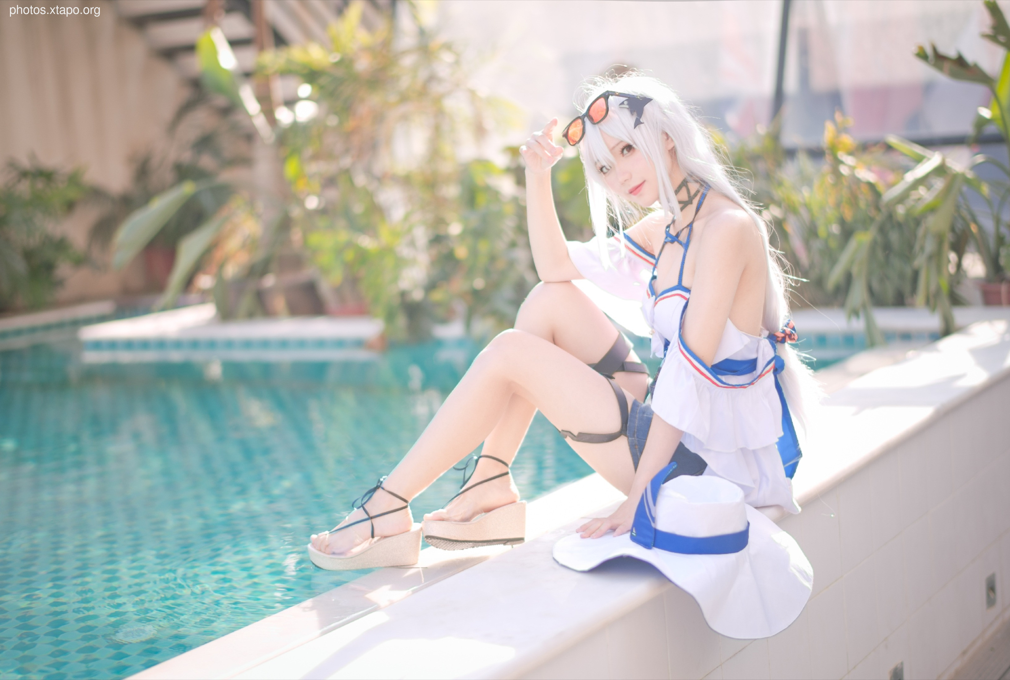 A stunning cosplay model poses by the pool in a summery outfit.  Her white and blue attire is complemented by a wide-brimmed hat and stylish sandals. The image features vibrant colors and a refreshing summer vibe.