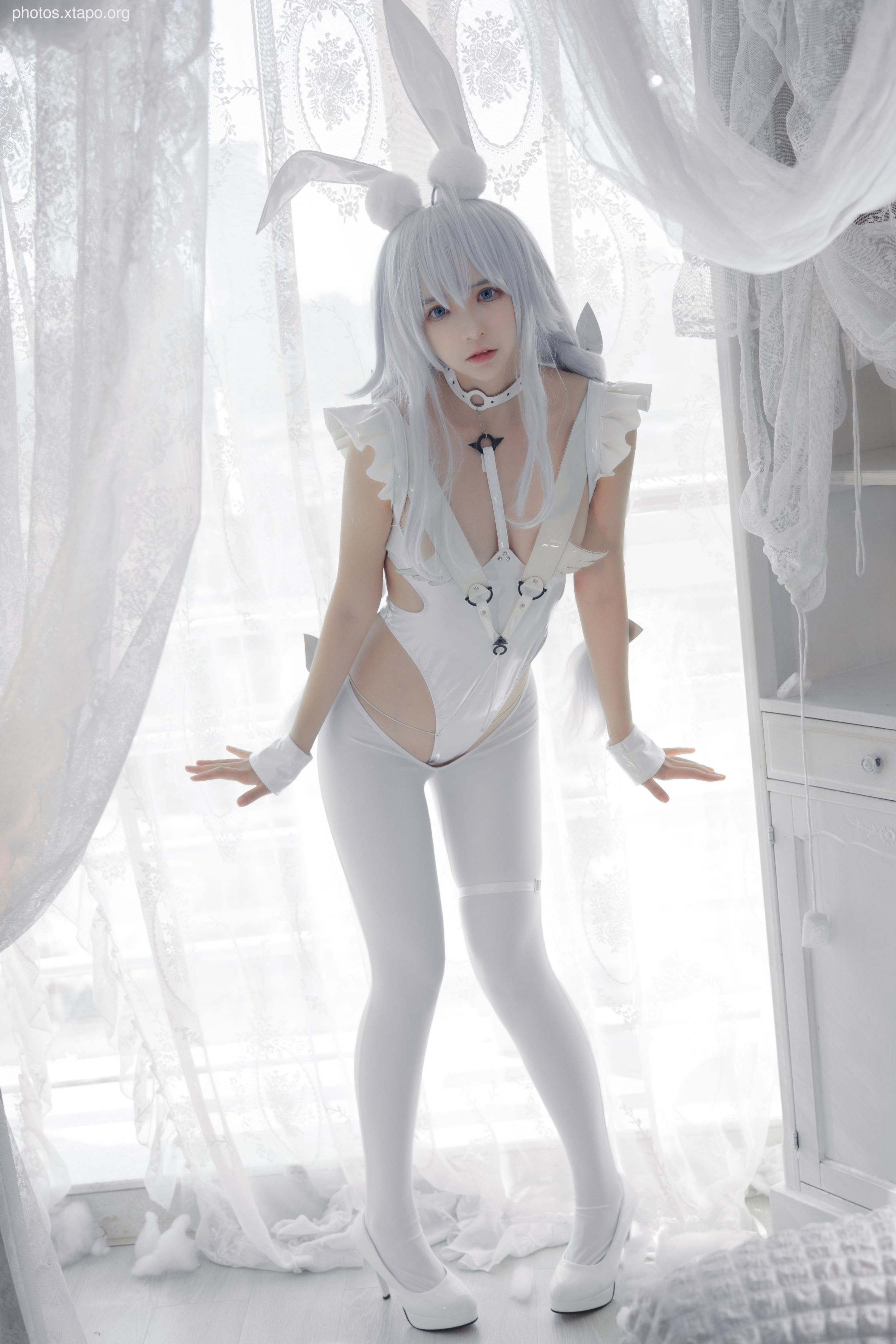 A young woman in a white bunny girl costume poses in a bright room.