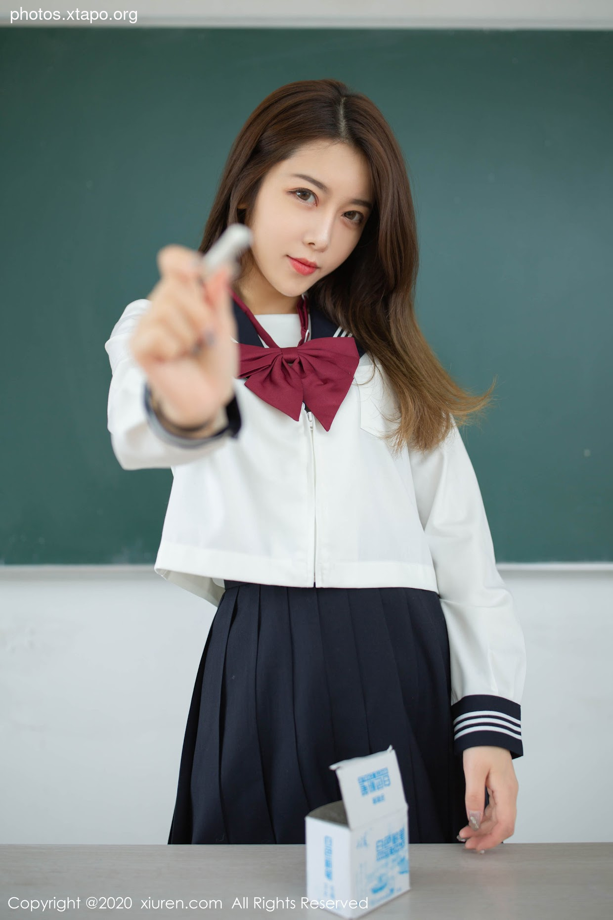 A schoolgirl in uniform holds a chalk, seemingly ready for a punishment.