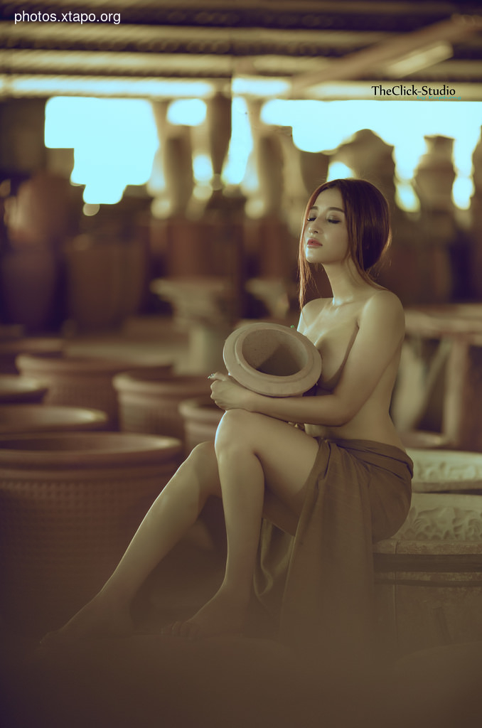 A woman sits peacefully amidst pottery, holding a clay vessel. The image evokes a sense of calm and artistry.