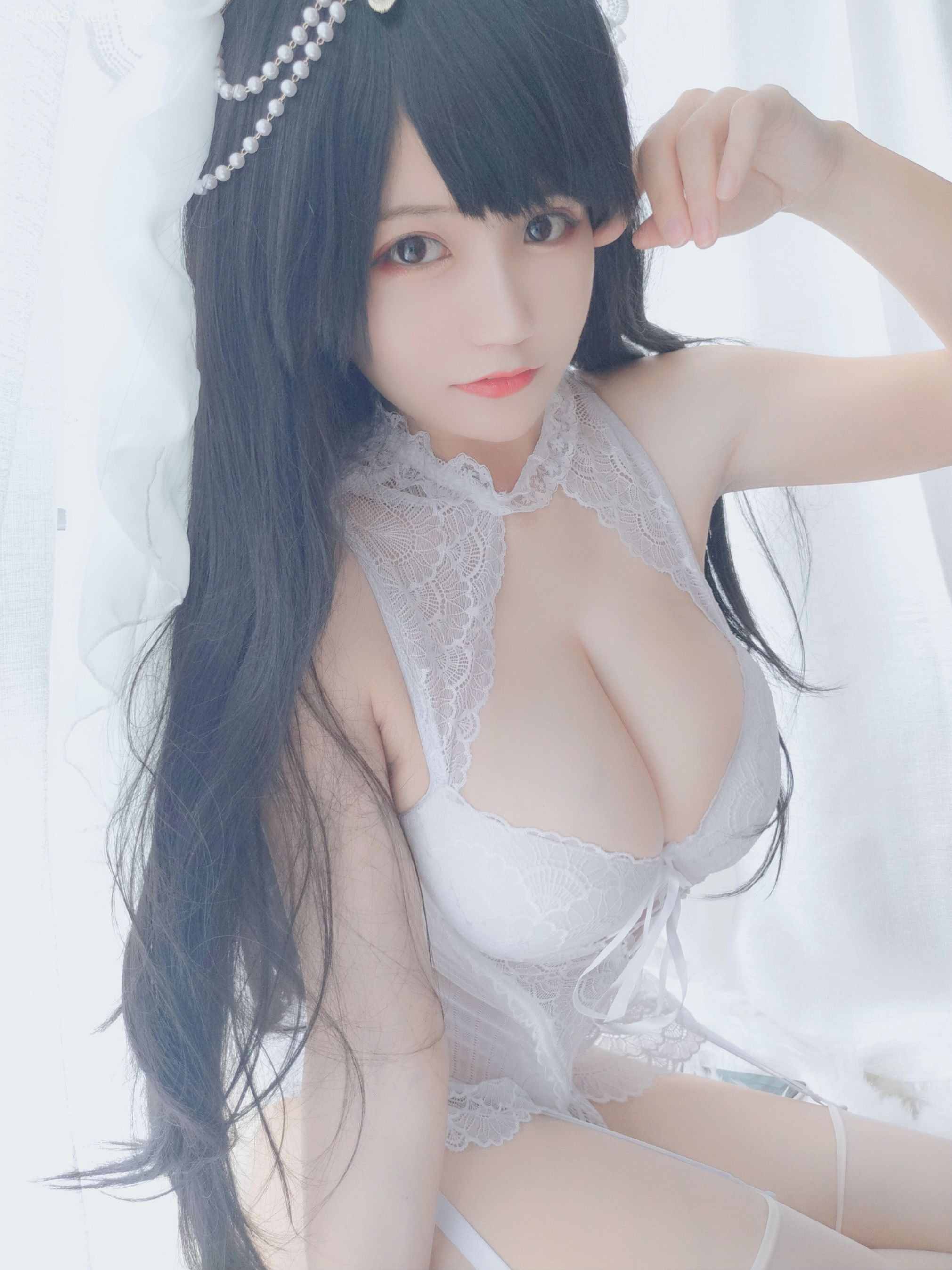 A young woman in a delicate white lace corset and garter belt poses for a photo. Her long, dark hair is styled elegantly, and she wears a pearl headband. The soft lighting and dreamy background enhance the romantic atmosphere.