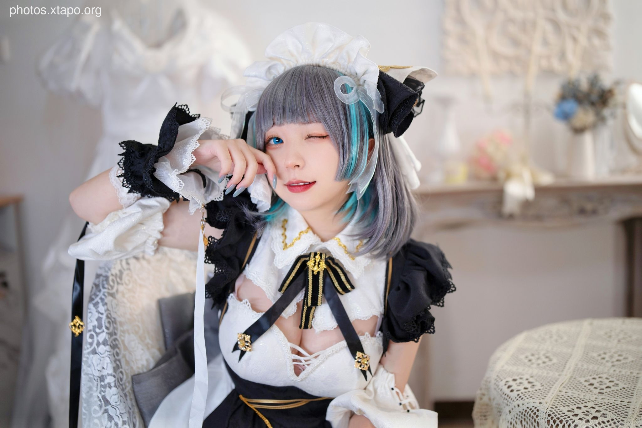 A cute girl cosplaying as a maid, winking playfully.  She's wearing a black and white maid outfit with lace details and has vibrant teal and gray hair.