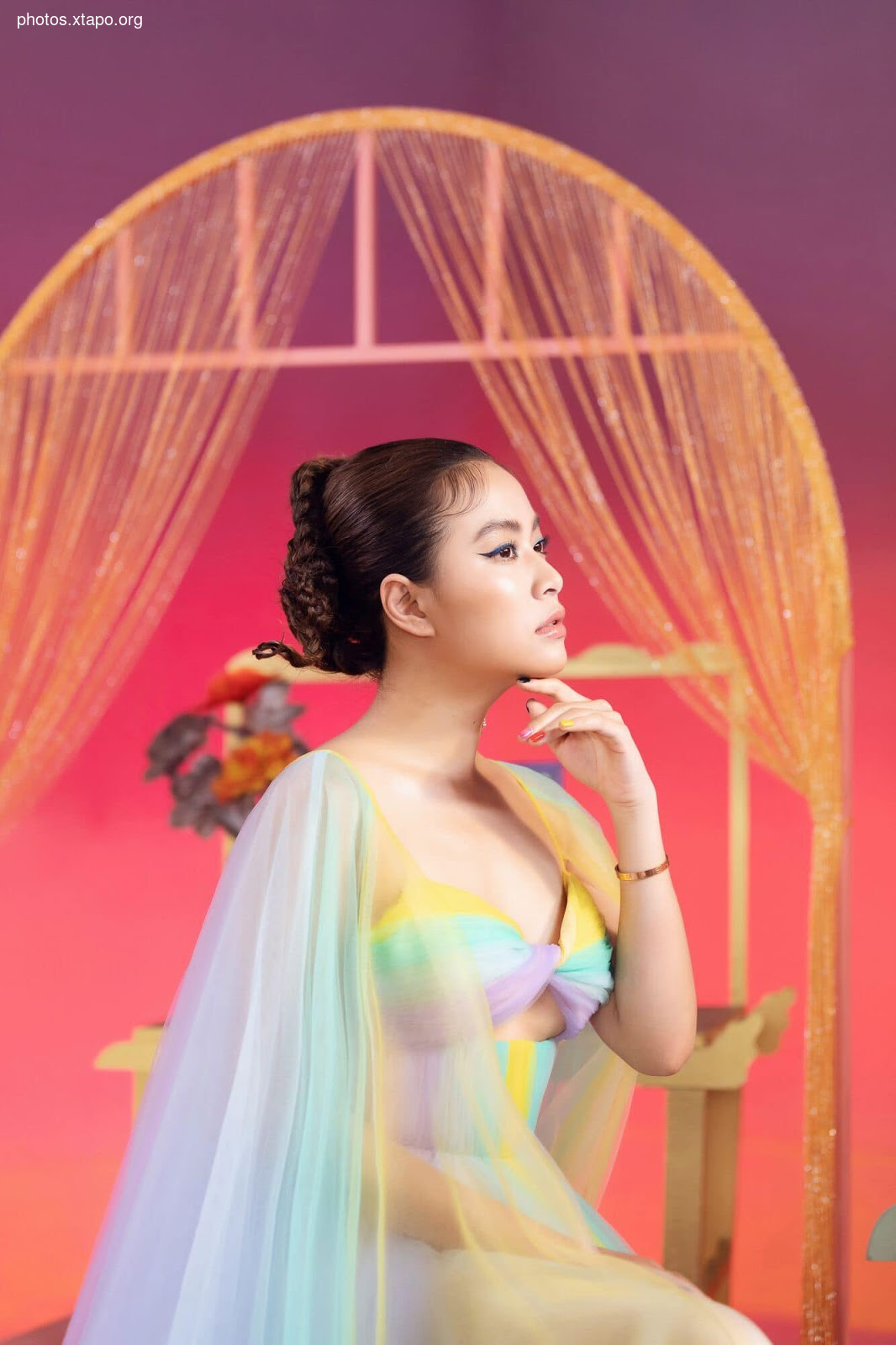 A woman in a pastel rainbow dress poses against a colorful backdrop.