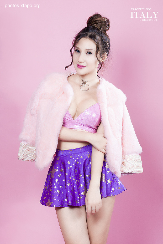 A young woman models a pink fur jacket and a purple star-print mini skirt. The image is set against a pink background.