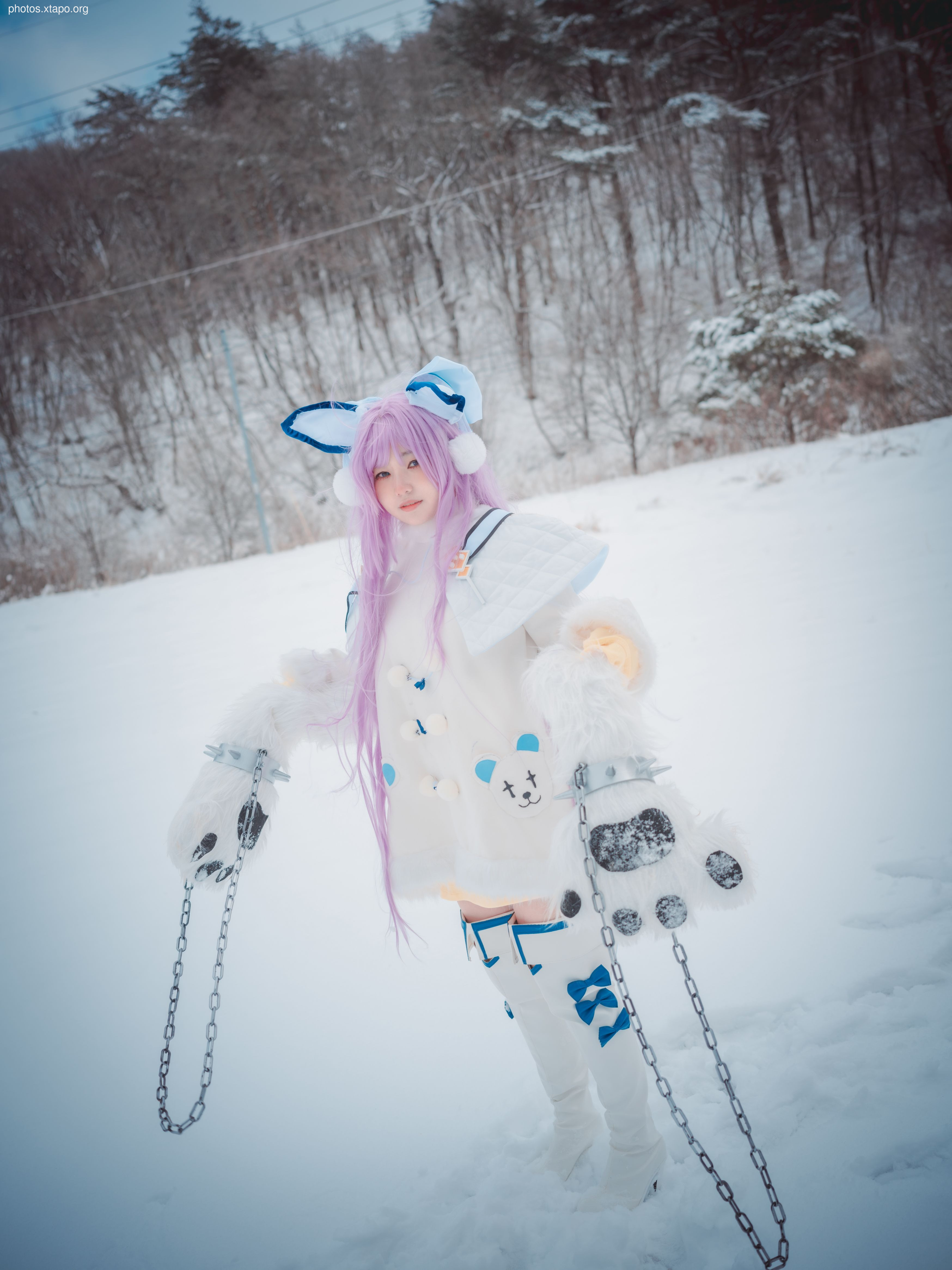 A cosplayer, dressed in a charming winter-themed costume, poses in a snowy landscape. The costume features a white dress with cute bear paw accessories and long purple hair. The image is perfect for showcasing the beauty of cosplay and winter scenery.