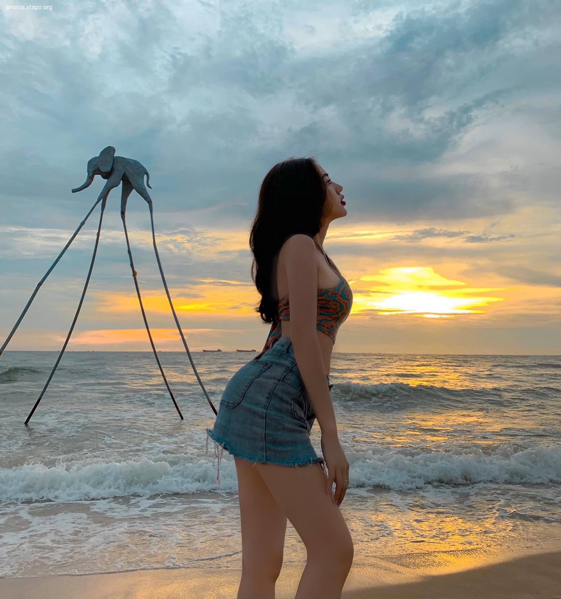 Young woman enjoying a sunset on the beach near an elephant sculpture.