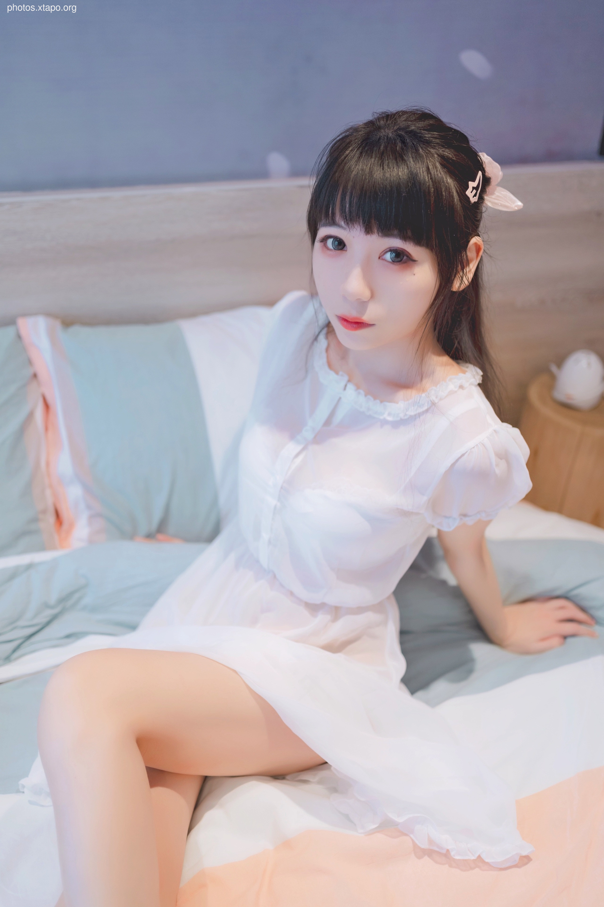 A young woman in a white dress relaxes on a bed.