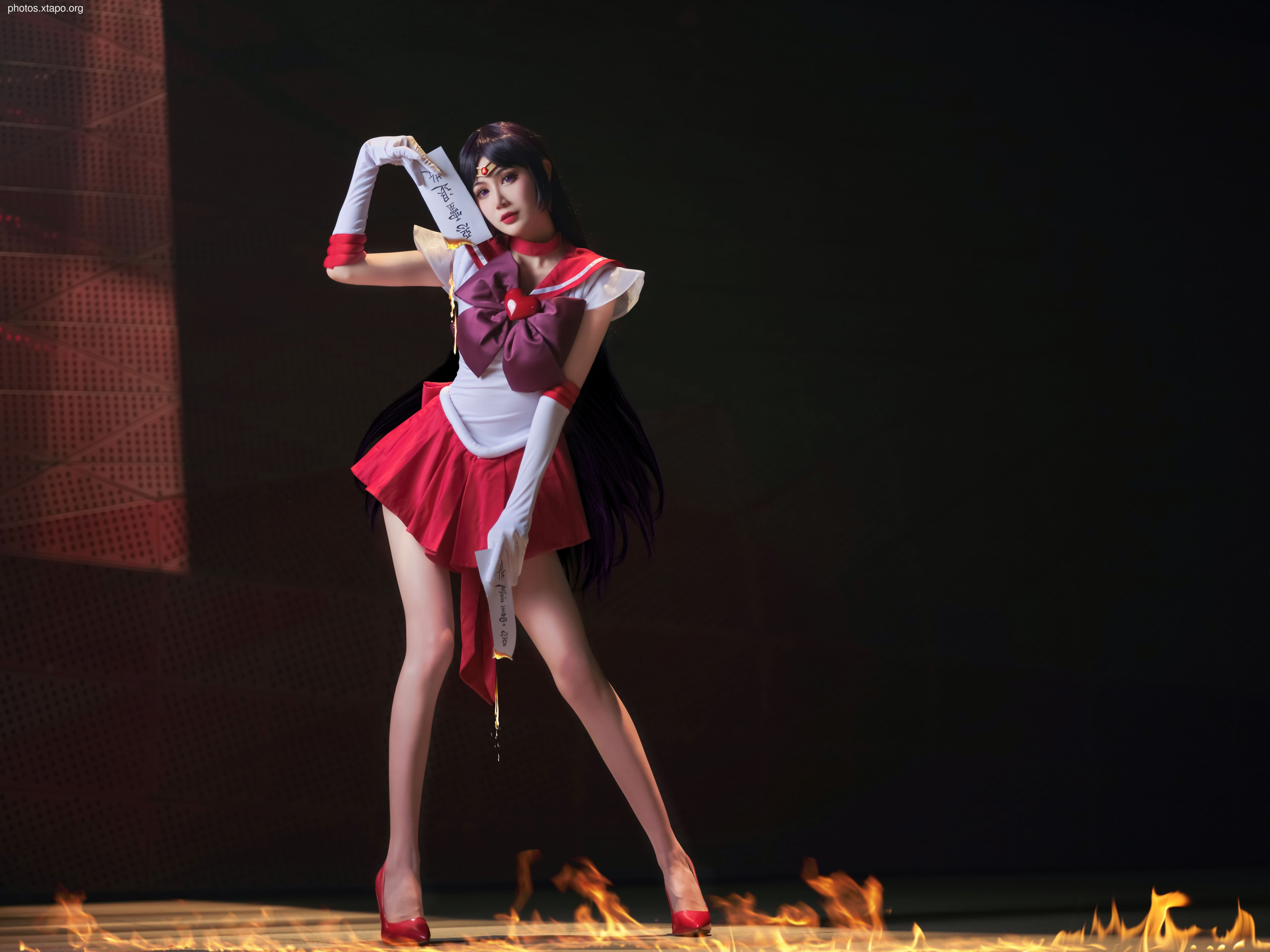A captivating portrayal of Sailor Mars, the fiery Sailor Senshi, standing amidst flames, holding a scroll.  Cosplay photography showcasing dramatic lighting and character detail.