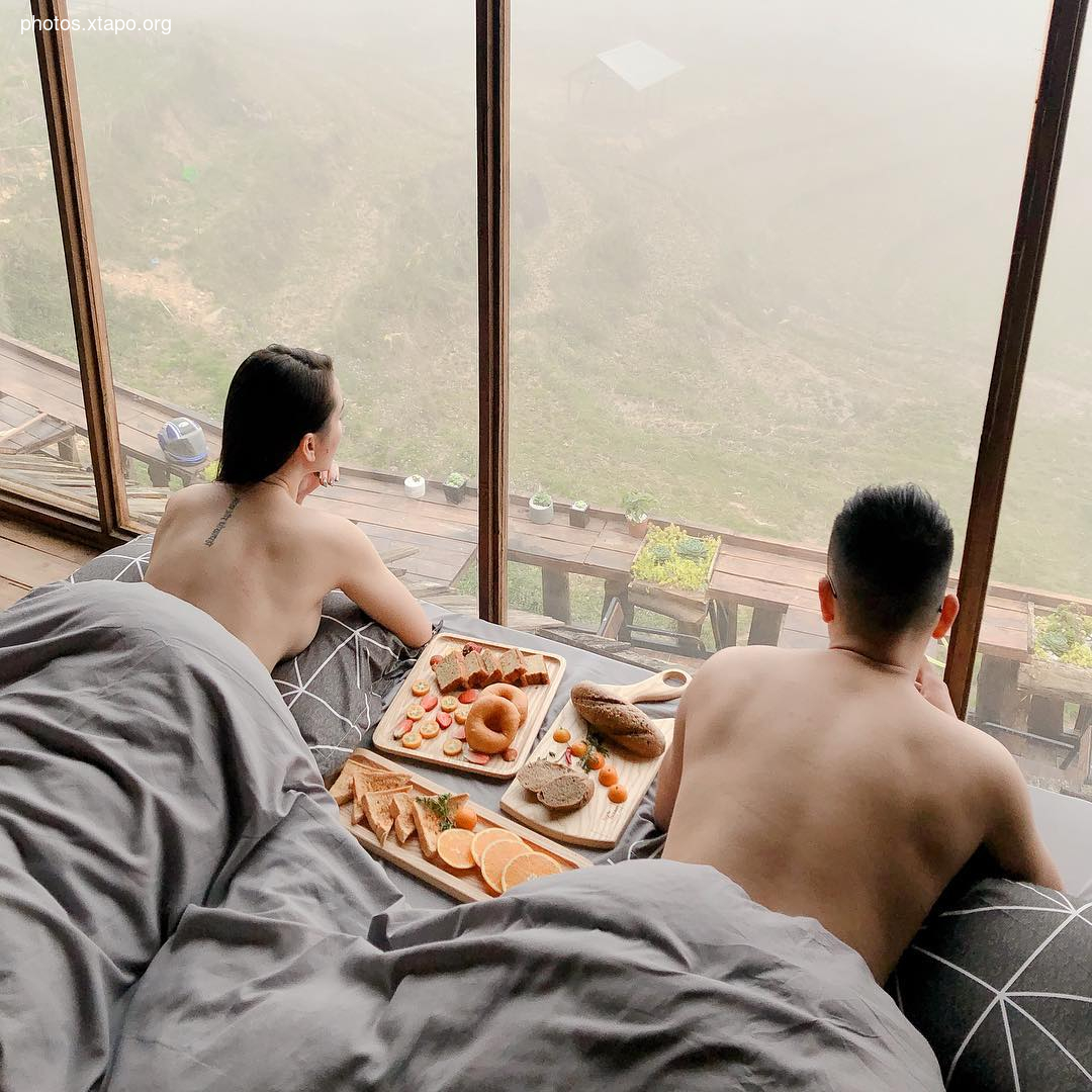 A couple enjoys a romantic breakfast in bed, overlooking a breathtaking foggy mountain vista.