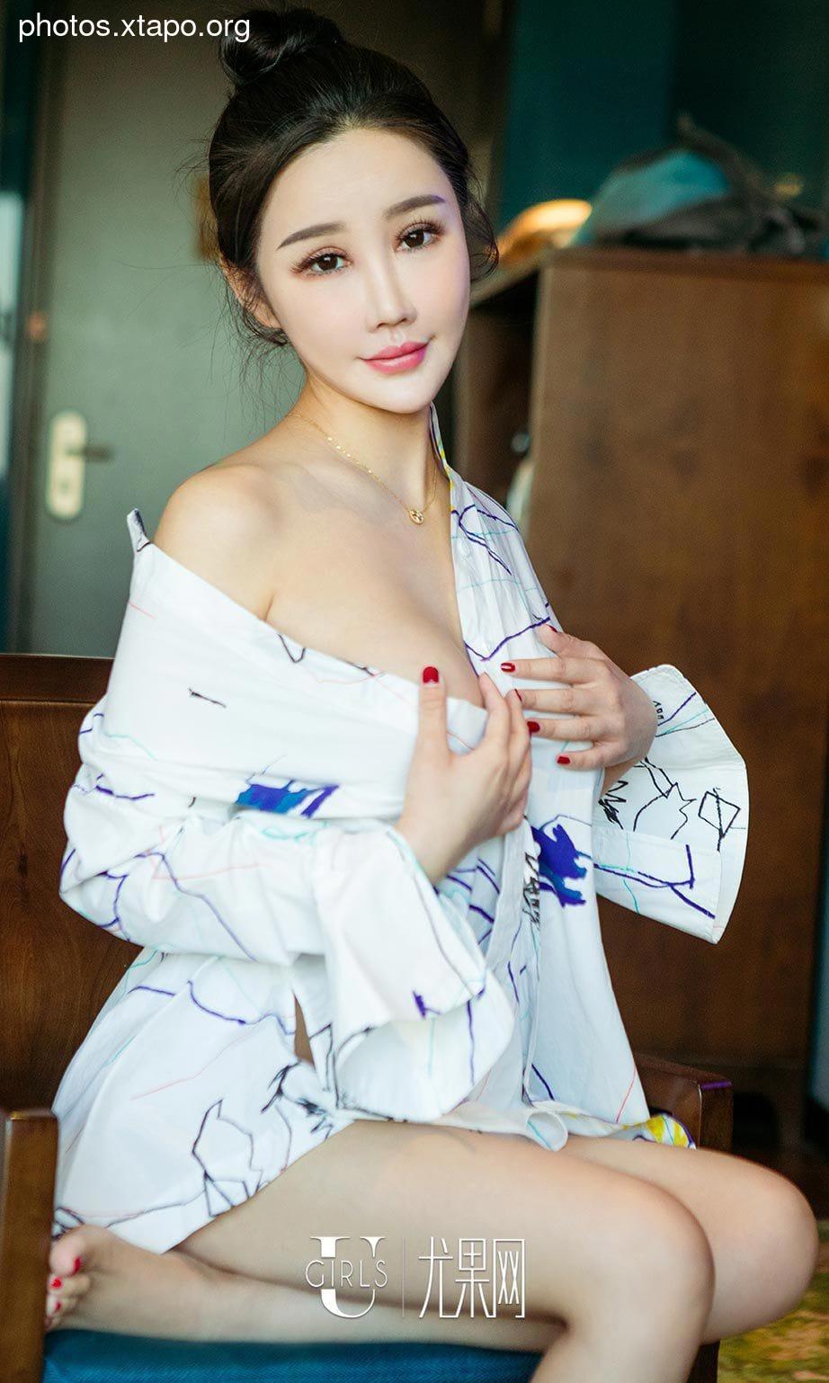 A stunning Asian woman with dark hair is captured in a close-up shot, elegantly dressed in a white, open-collared shirt with abstract designs. Her captivating gaze and subtle smile add to the allure of the image.