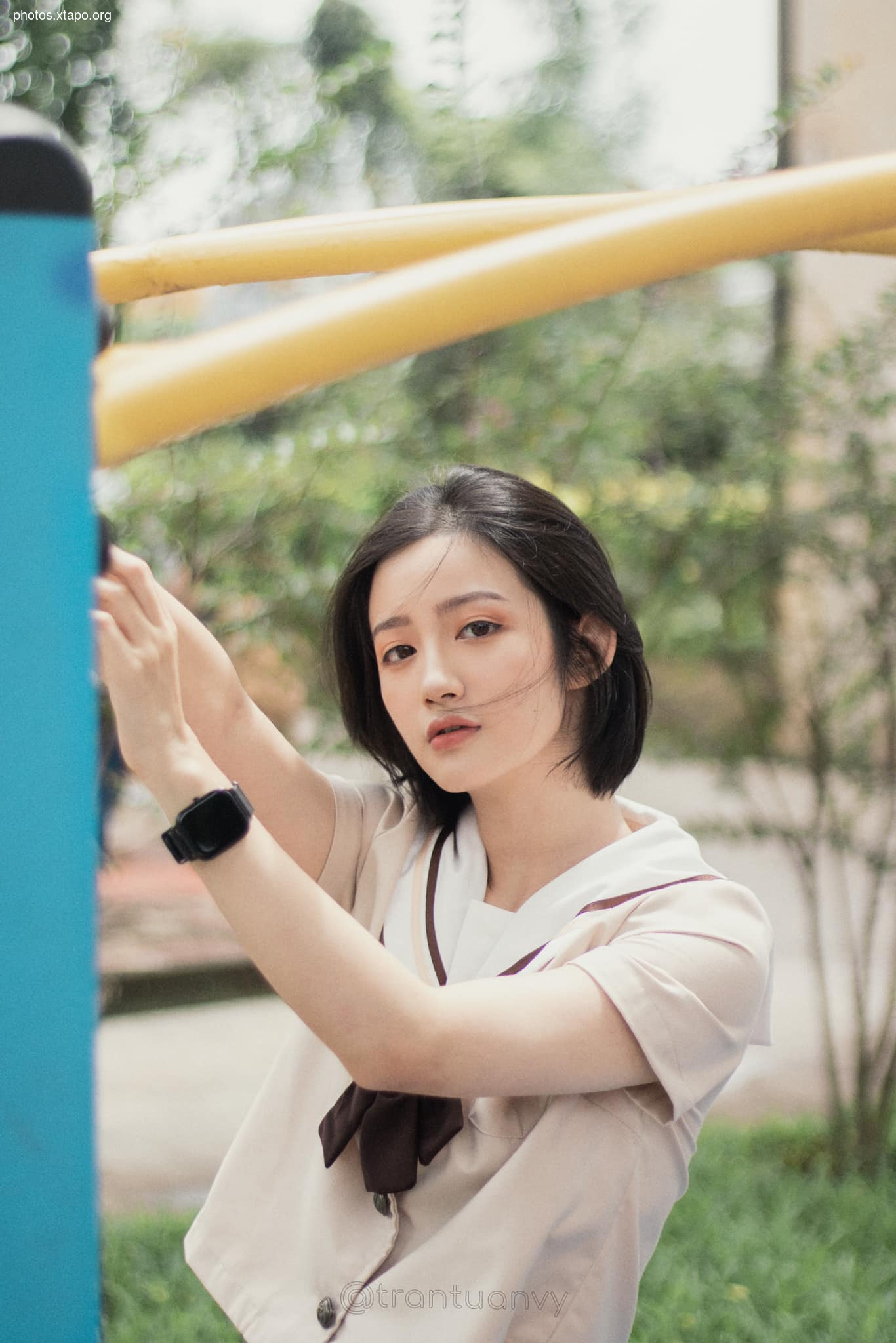A young woman in a school uniform playfully interacts with outdoor exercise equipment.