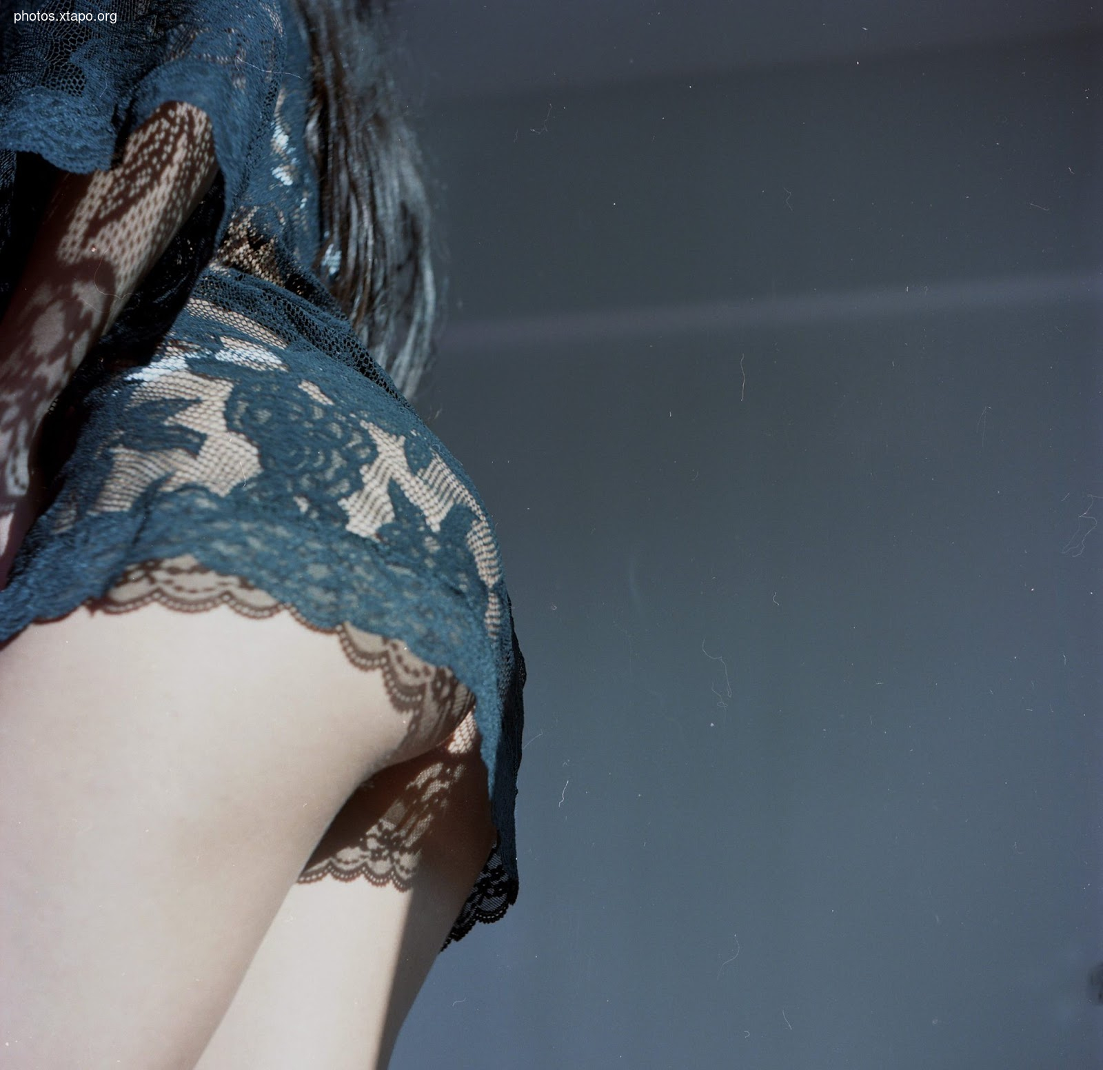 Close-up of a woman's back wearing a dark teal lace dress. The image is slightly grainy, suggesting it may be a photograph.