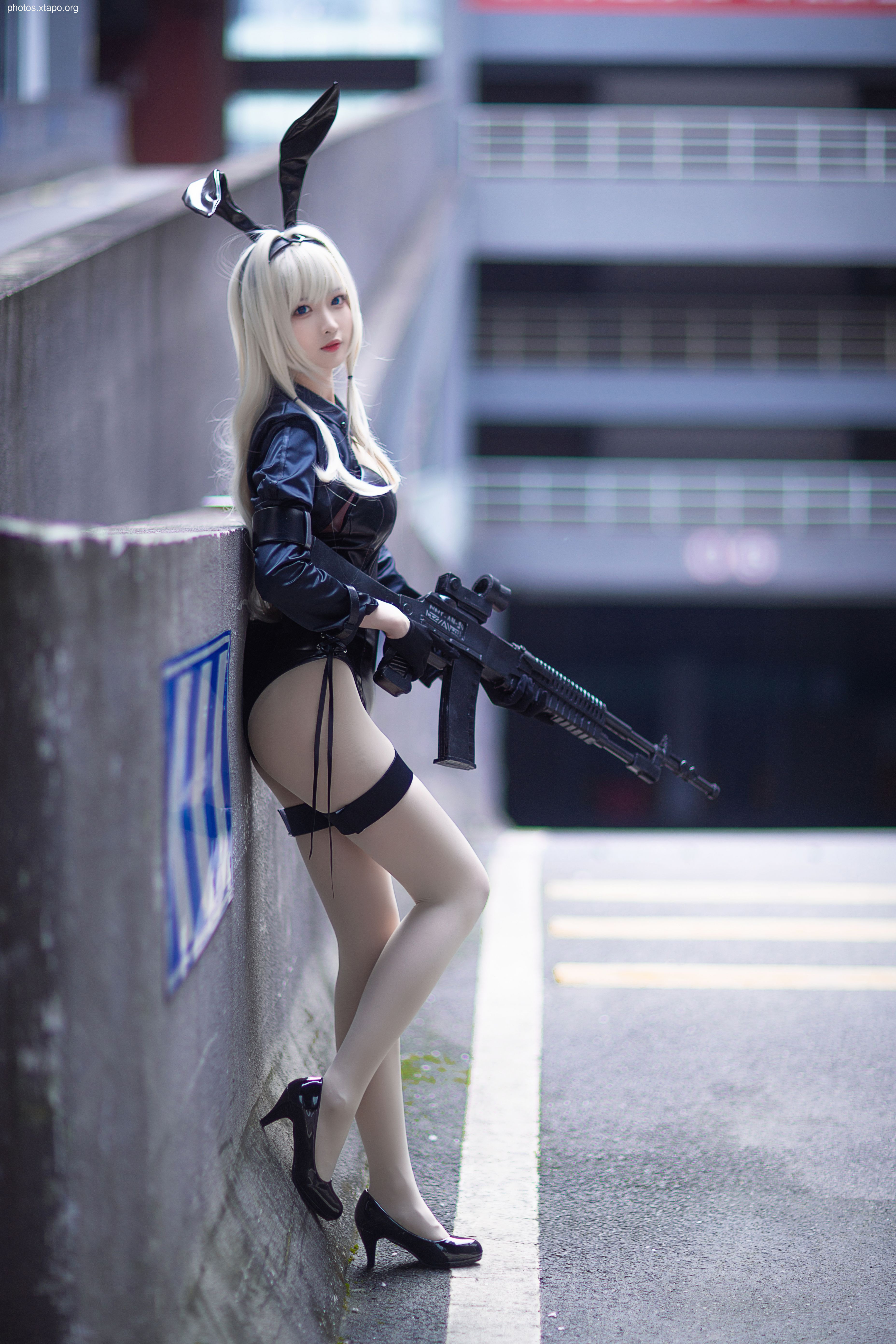 A cosplayer strikes a pose in a parking garage. She wears a black bodysuit, bunny ears, and high heels, and holds a rifle. This stylish and edgy look blends tactical gear with playful elements.