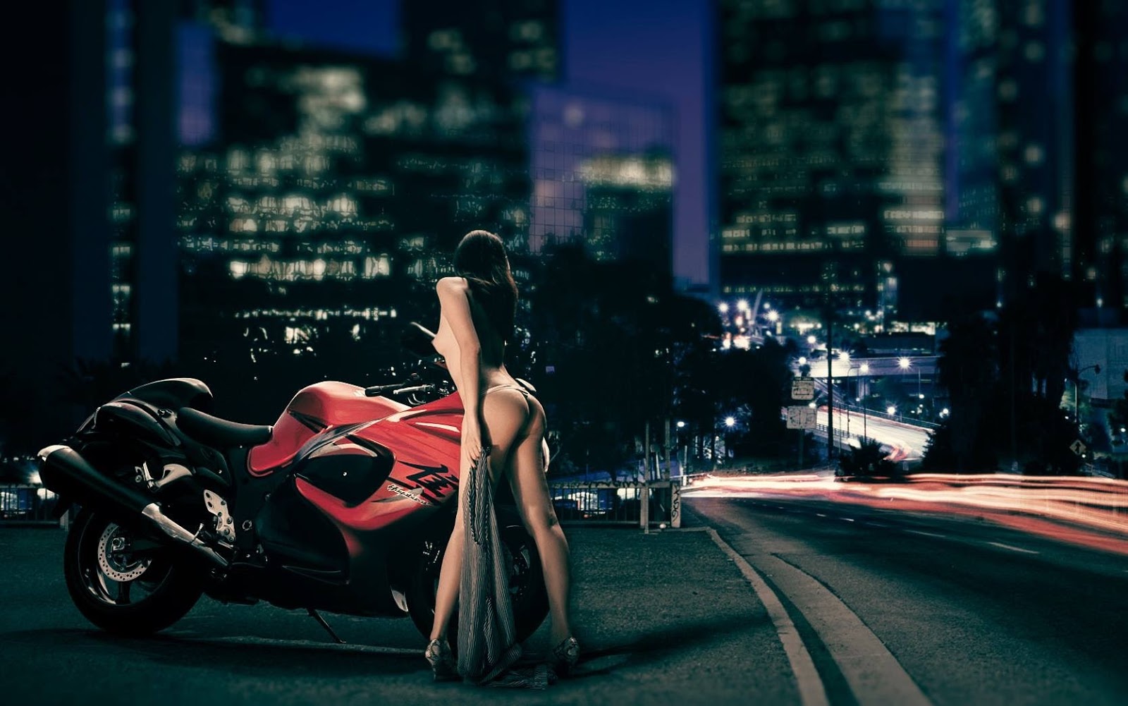 A woman stands beside a red motorcycle at night in the city.