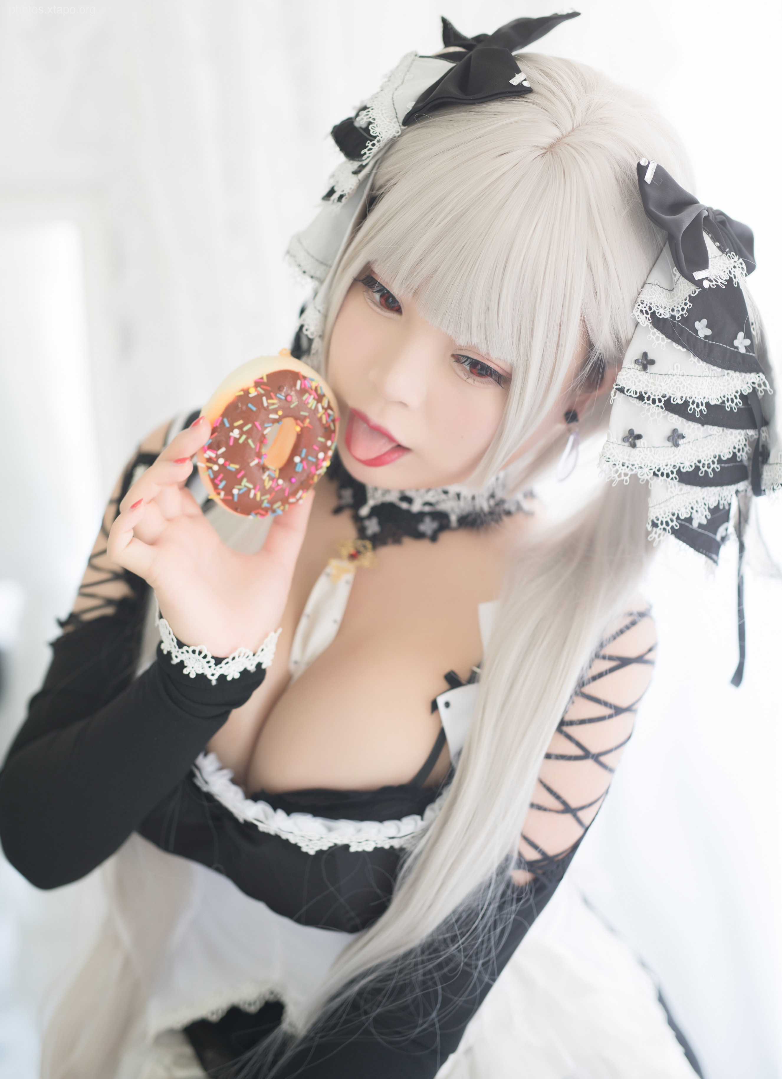 A young woman in a gothic lolita cosplay outfit enjoys a donut.  She has long silver hair and is wearing a black and white dress.