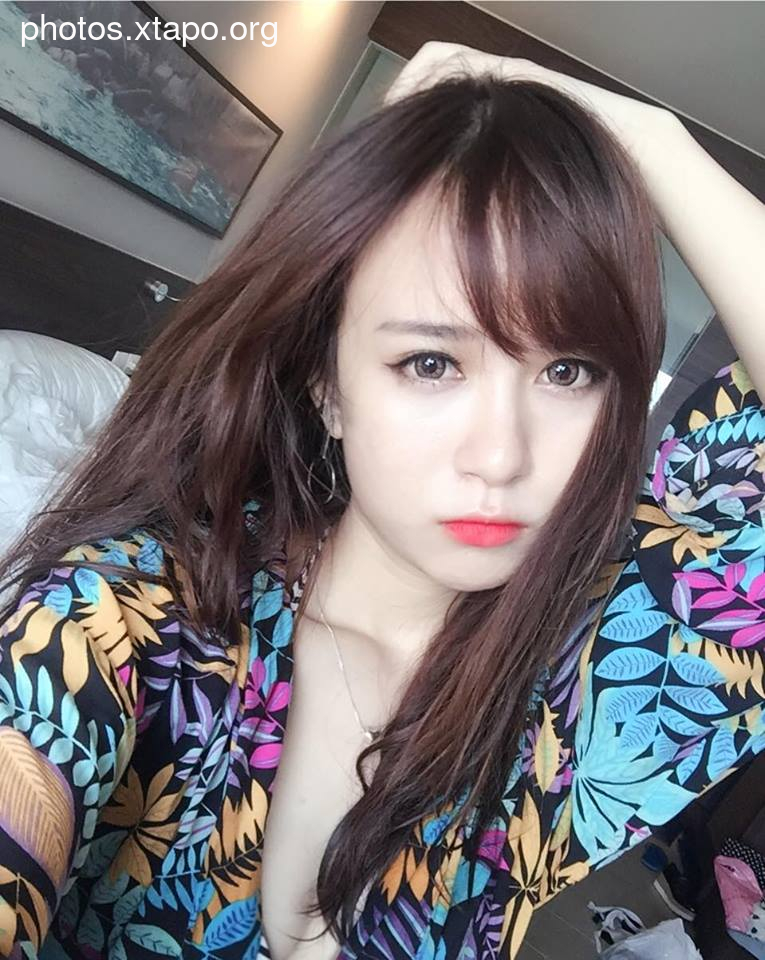 A young woman with long brown hair poses for a selfie. She is wearing a colorful floral shirt.