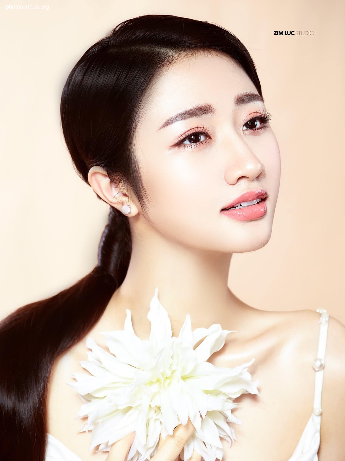 Portrait of a young woman with flawless skin and a delicate white flower.  Professional makeup and hair styling.