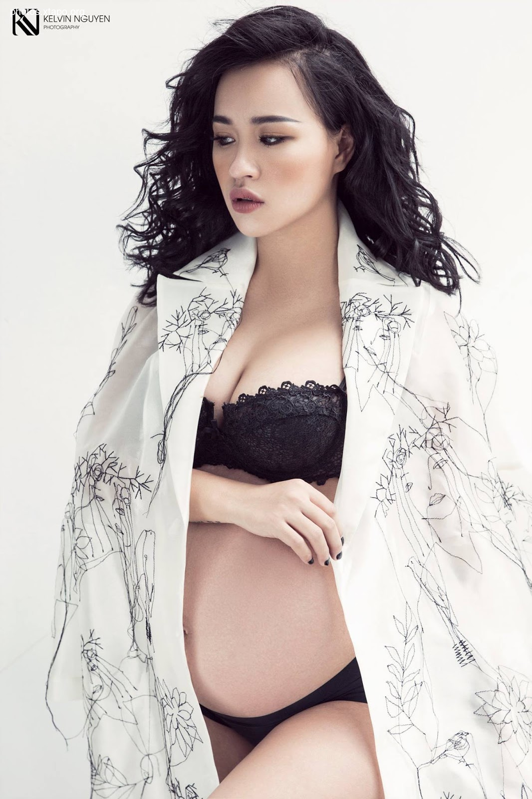 A beautiful pregnant woman poses in a flowing white robe adorned with delicate line art.  The image evokes a sense of serenity and anticipation.