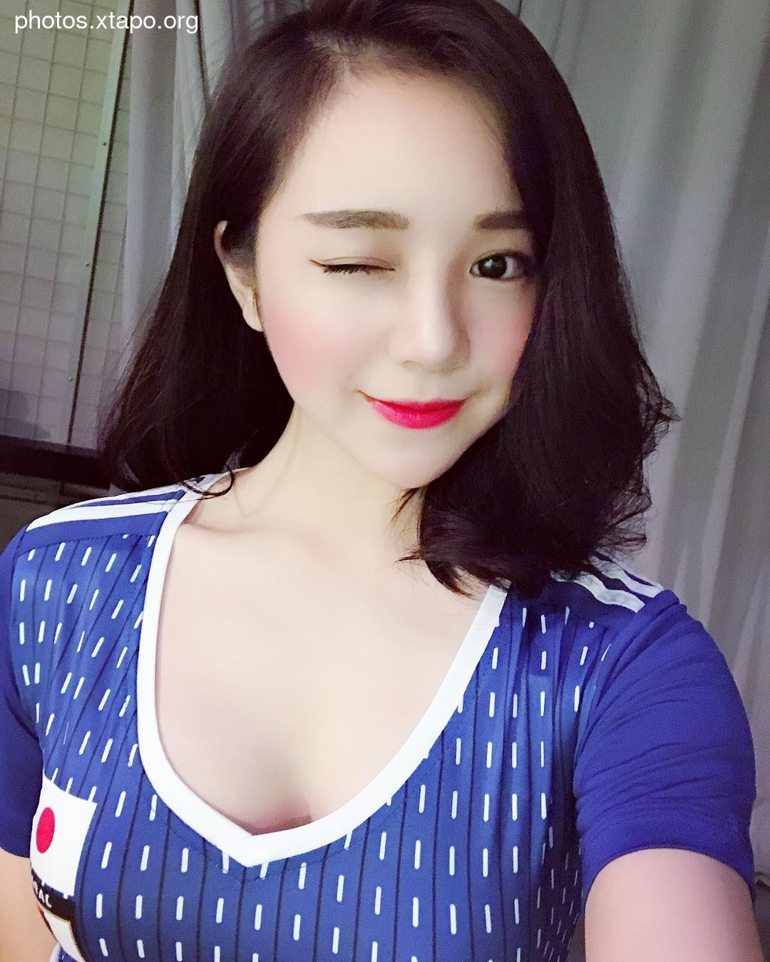 A woman winks at the camera while wearing a blue and white patterned jersey.