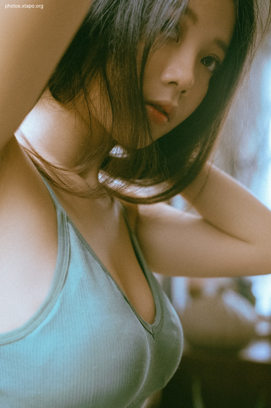 A woman with long dark hair is shown from the shoulders up. She is wearing a teal-colored top. The image is soft and has a vintage feel.