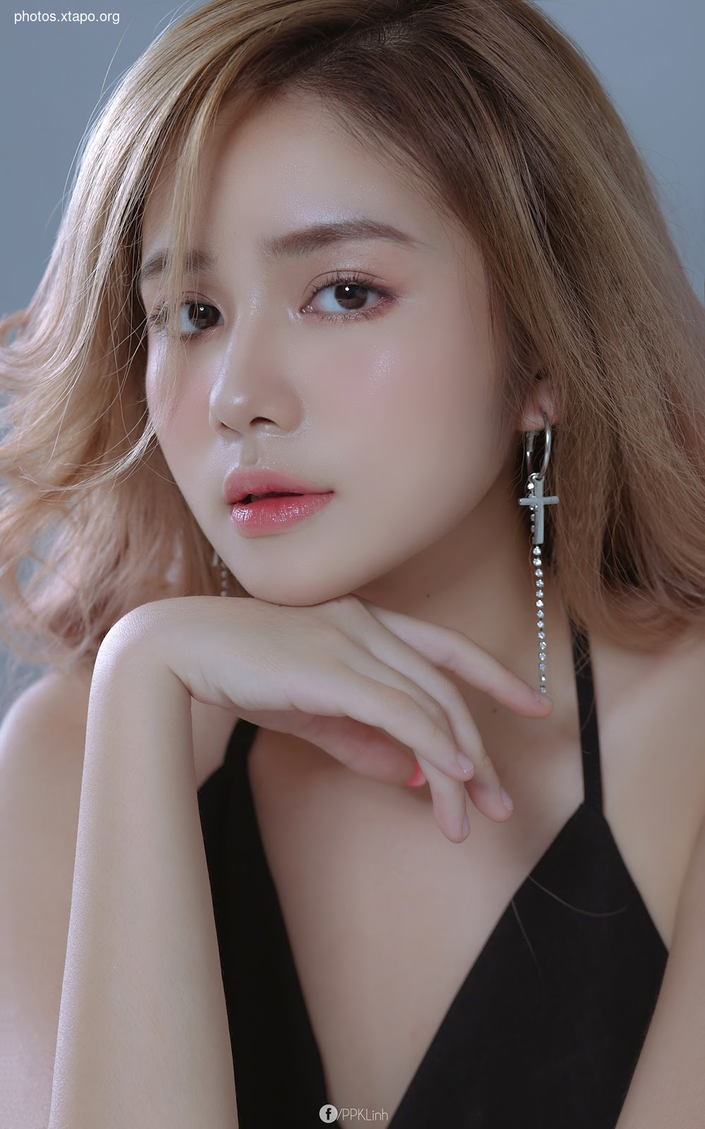 Portrait of a young woman with long brown hair, wearing a black dress and cross earrings. She is looking at the camera with a soft expression.