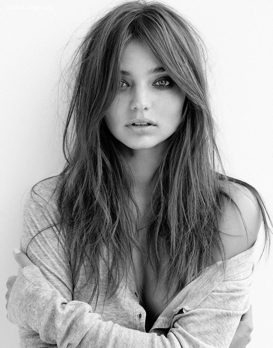 Black and white portrait of a young woman with long, slightly messy hair. She is wearing a simple gray cardigan and has a pensive expression.
