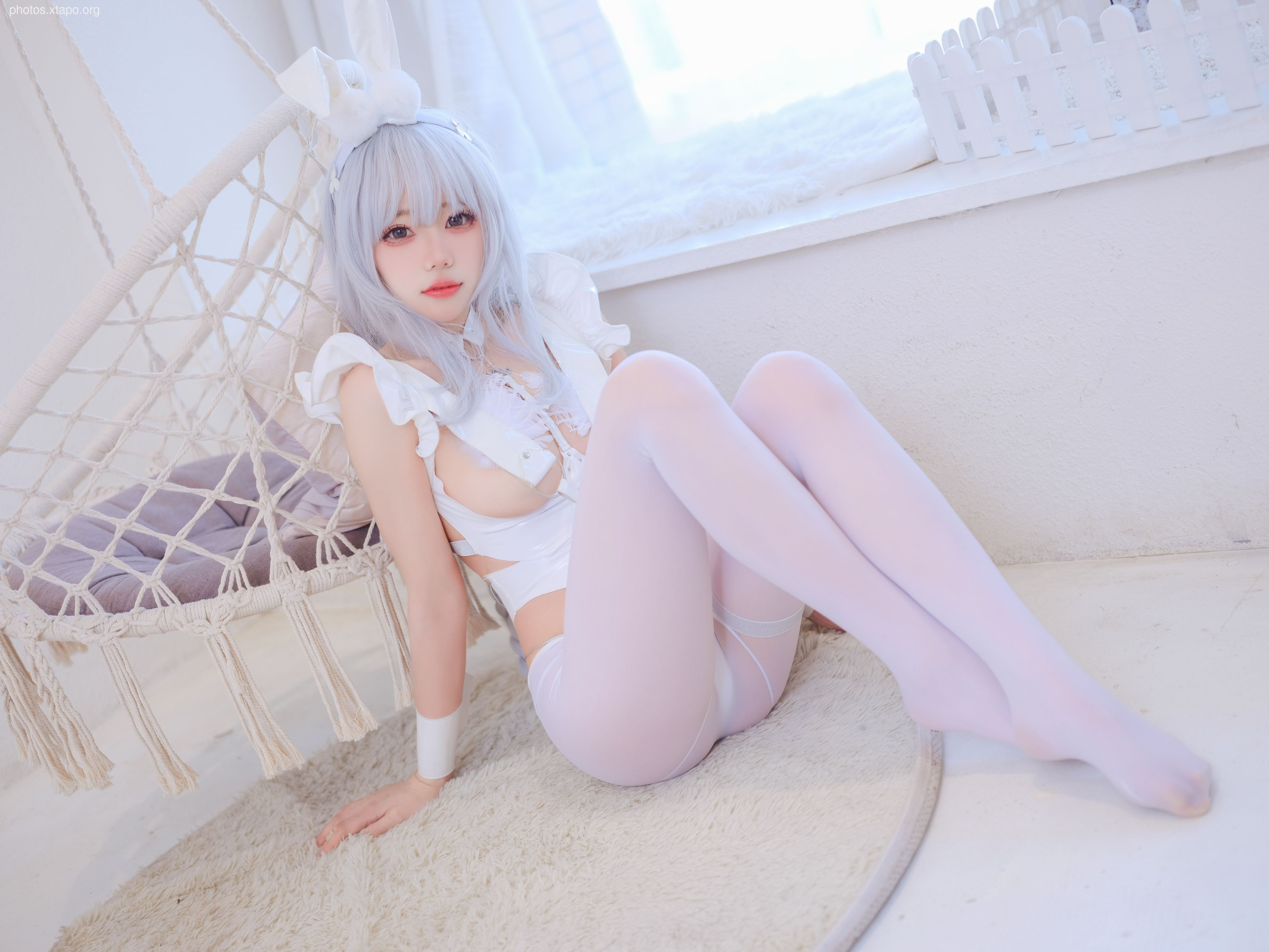 A young woman in a white bunny girl costume poses for a photograph.  She is wearing white tights and a white top. The setting is bright and airy.