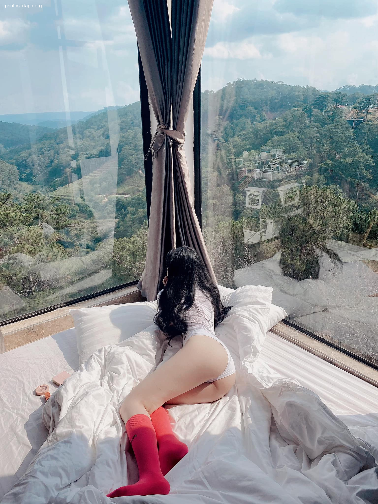 Woman enjoying a relaxing moment in bed with a stunning mountain view from a large window.