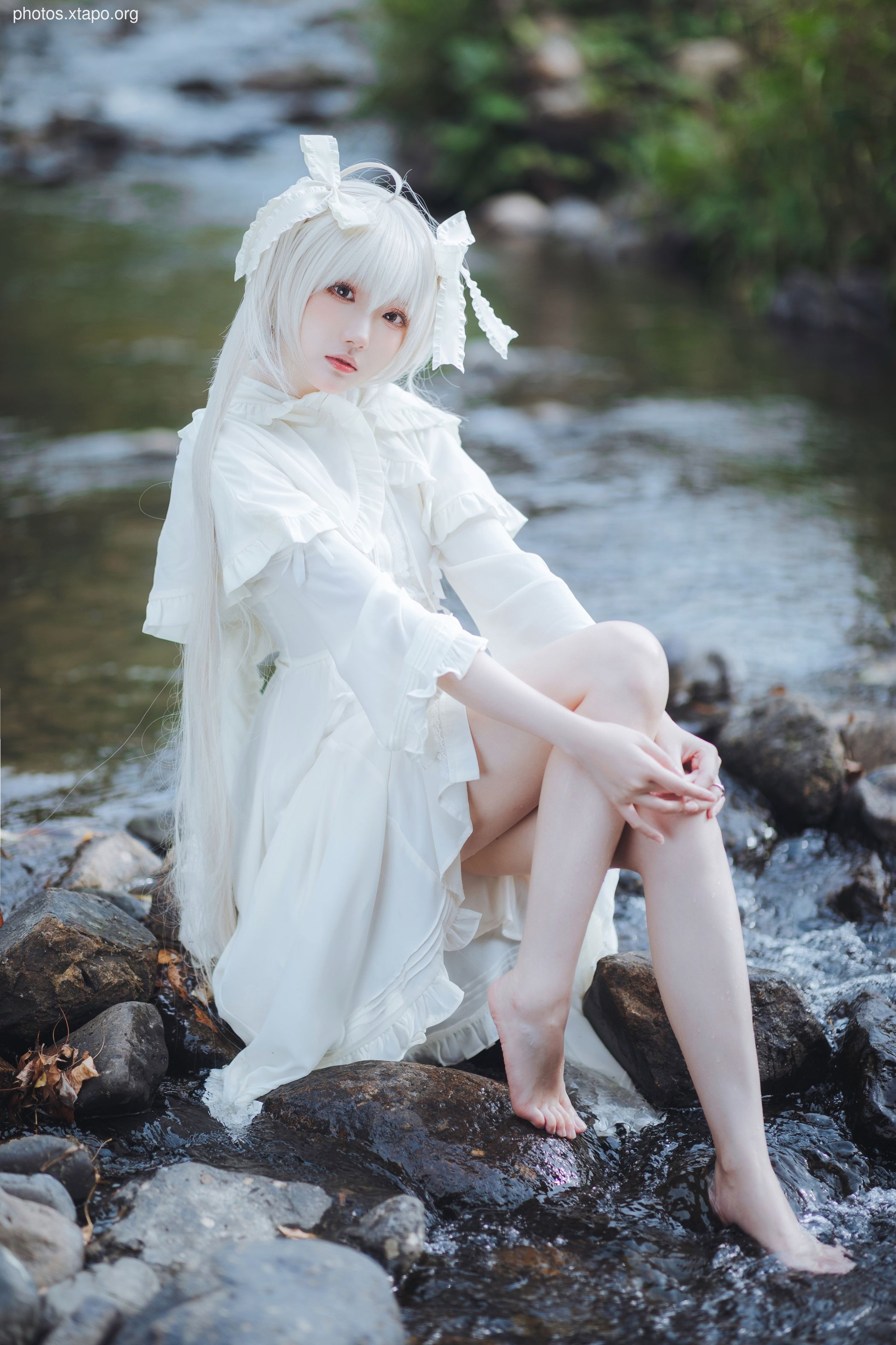 A captivating cosplay photoshoot of a young woman in a white dress by a creek. Her elegant pose and serene expression create a magical atmosphere.