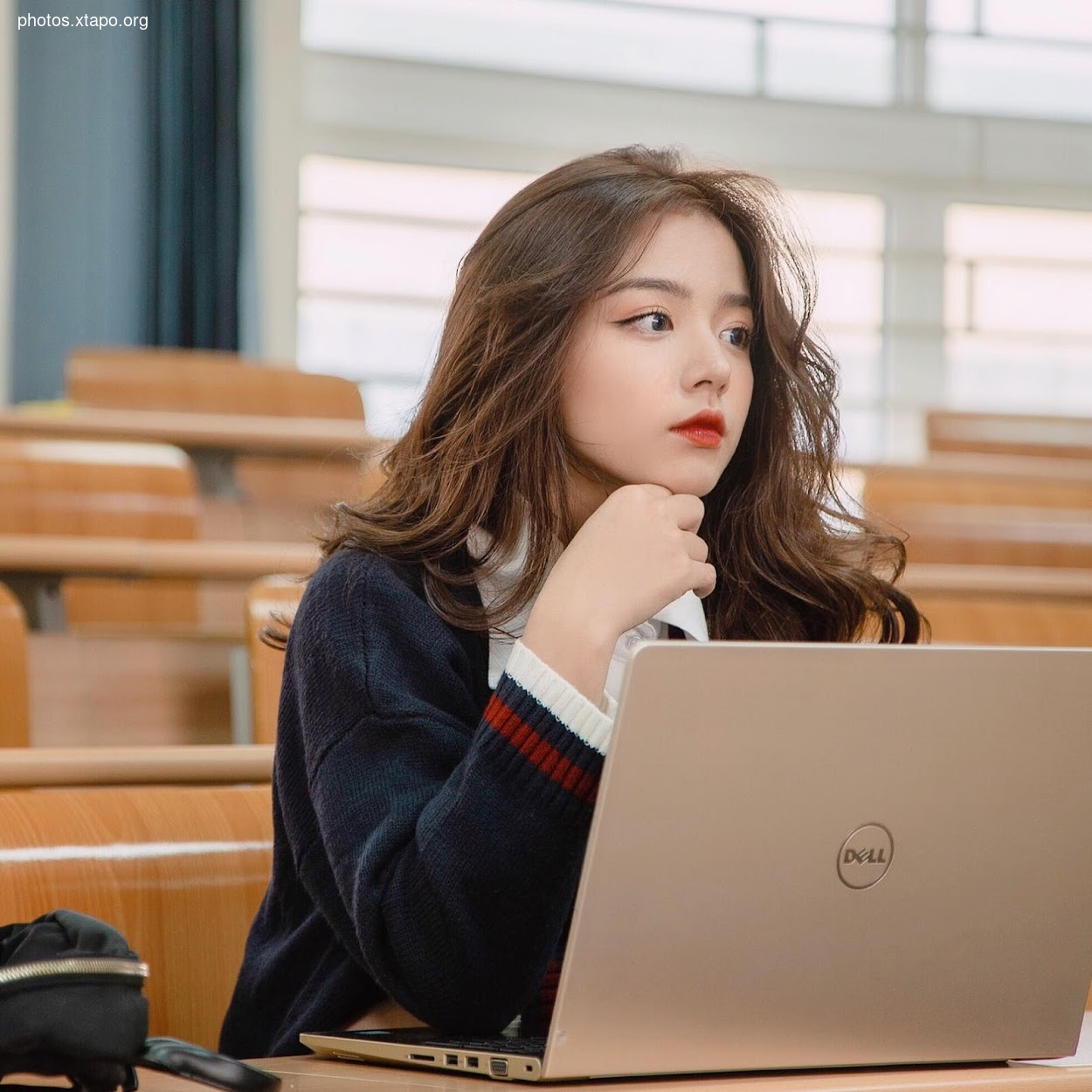 A young woman sits in a lecture hall, thoughtfully working on her Dell laptop.
