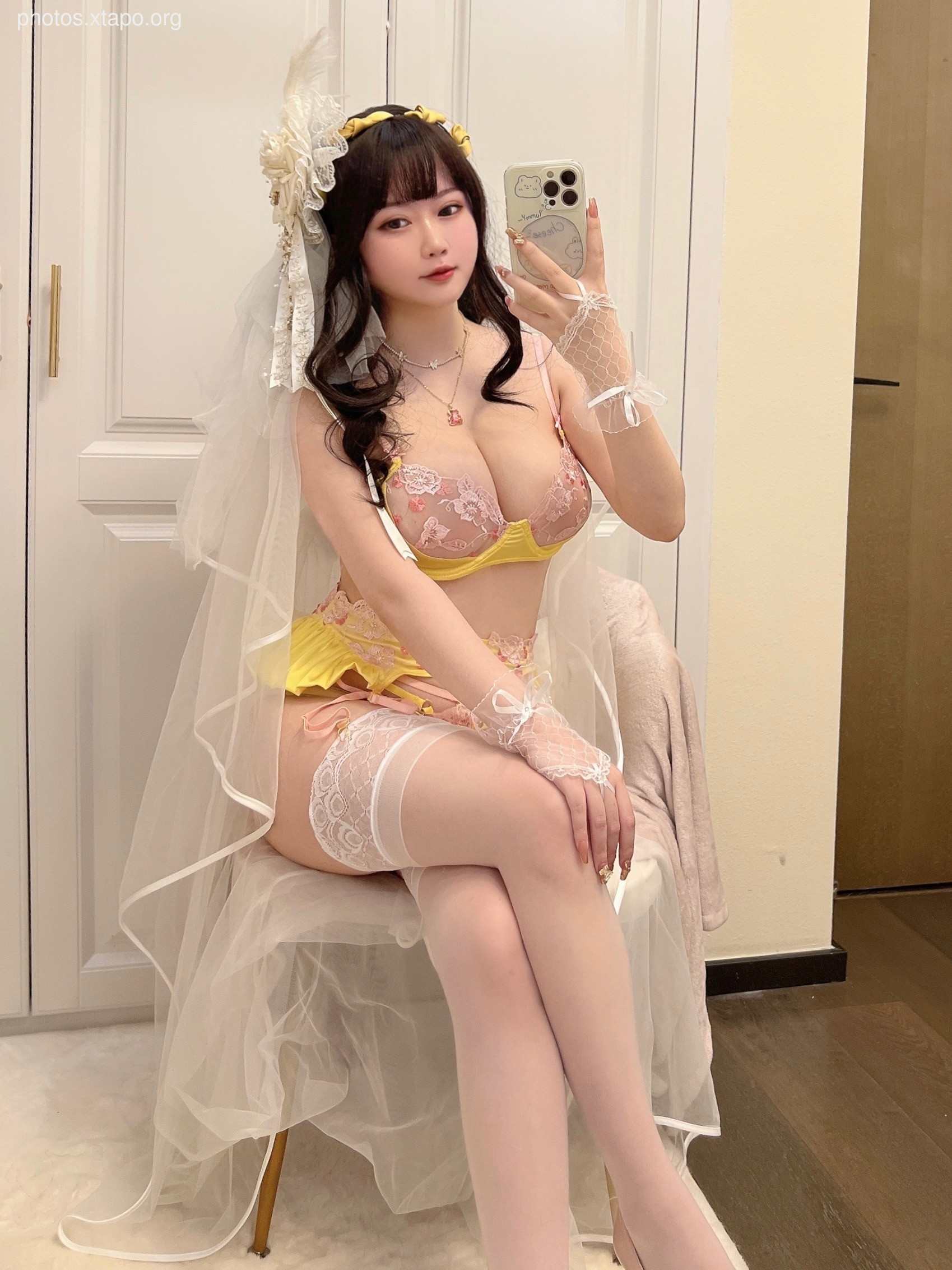 A woman in a yellow and pink lingerie set poses for a selfie while wearing a white veil.