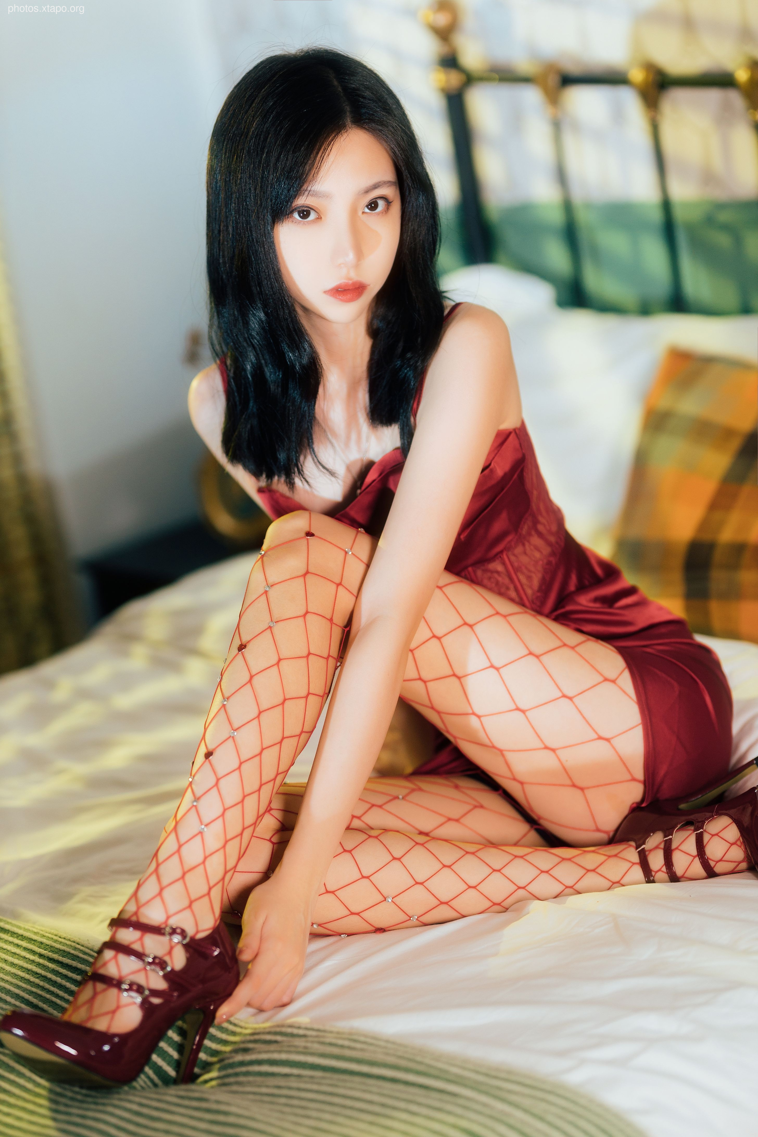 A captivating young woman poses elegantly in a crimson dress and fishnet stockings, exuding confidence and allure.