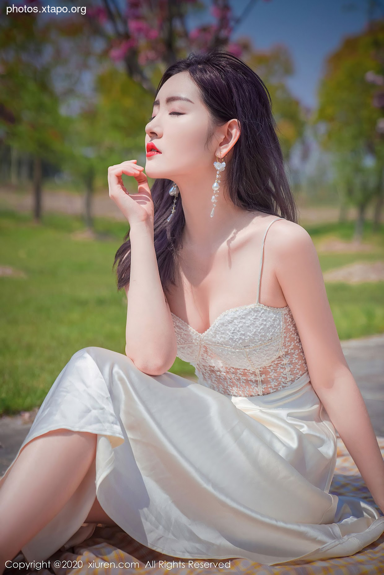 A young woman in a white dress sits in a park, enjoying the sunshine.
