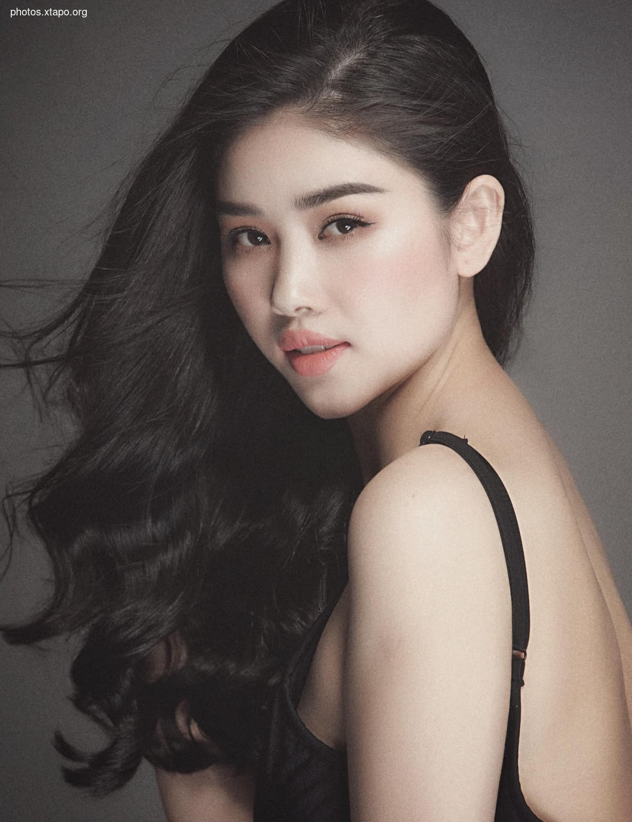 Portrait of a young woman with long, dark hair. She is wearing a black top and has a soft, natural look.