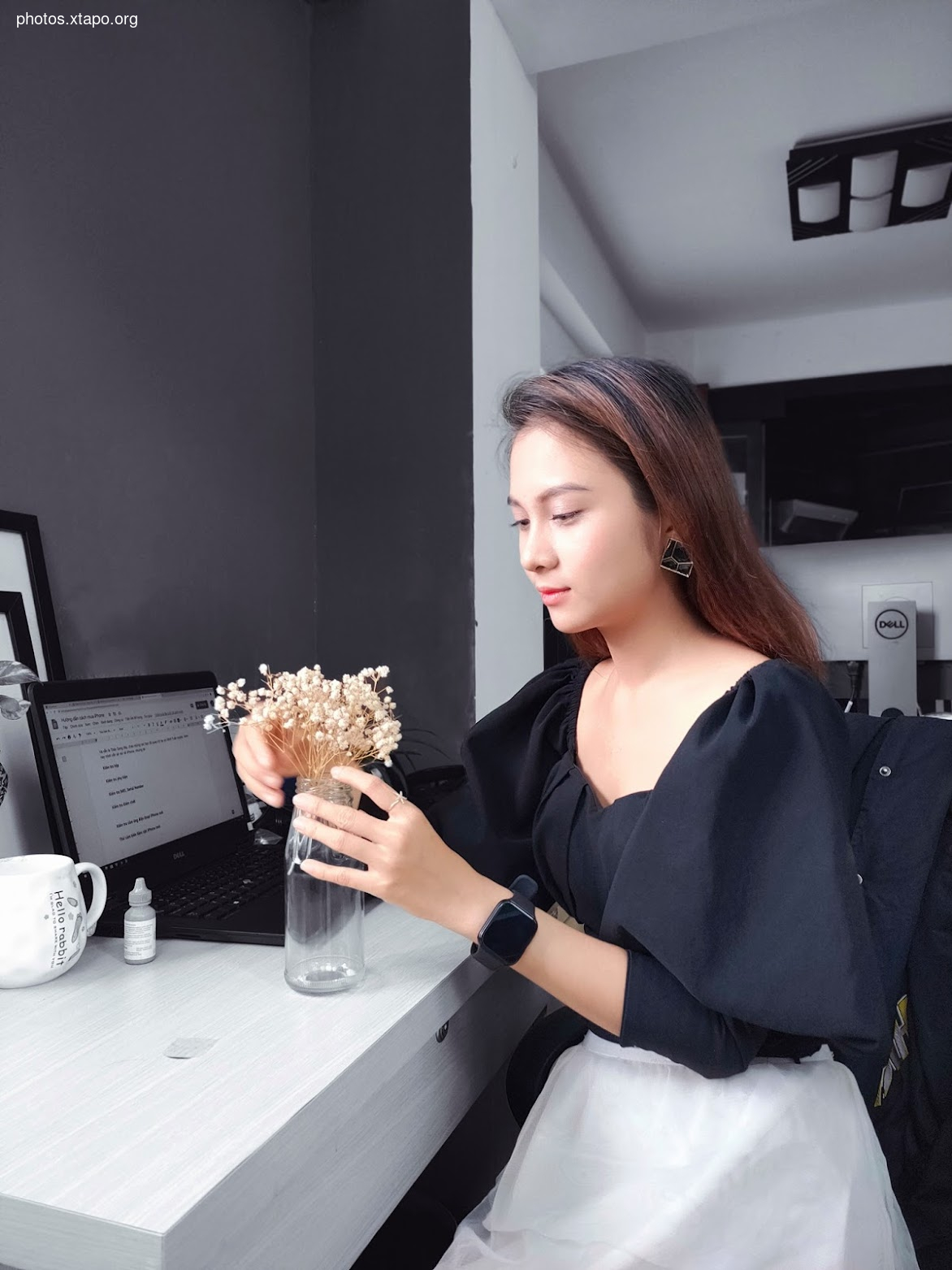A young woman sits at her desk, working on her laptop. She has a small bouquet of dried flowers in front of her.