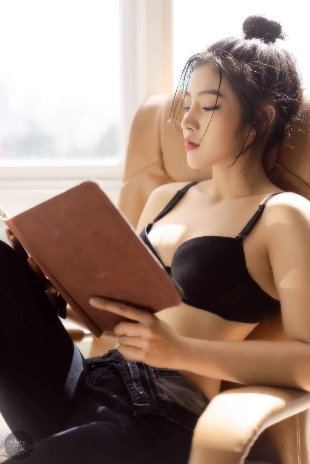 A young woman sits in a chair by a window, engrossed in a book.