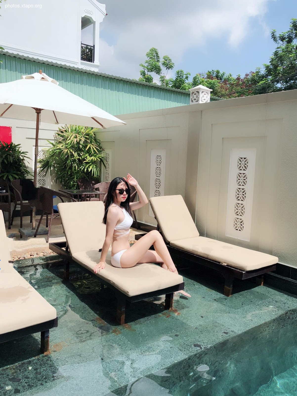 A woman in a white bikini relaxes by the pool on a sunny day.