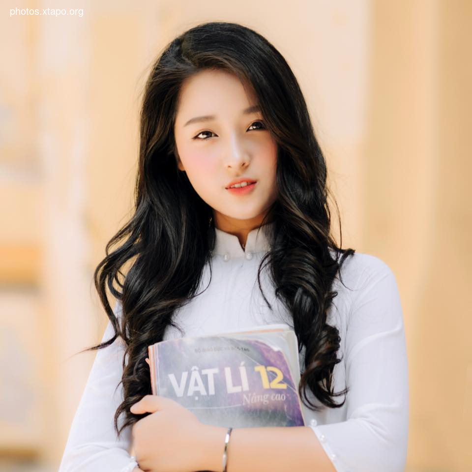 A young Vietnamese woman with long black hair holds a physics textbook.